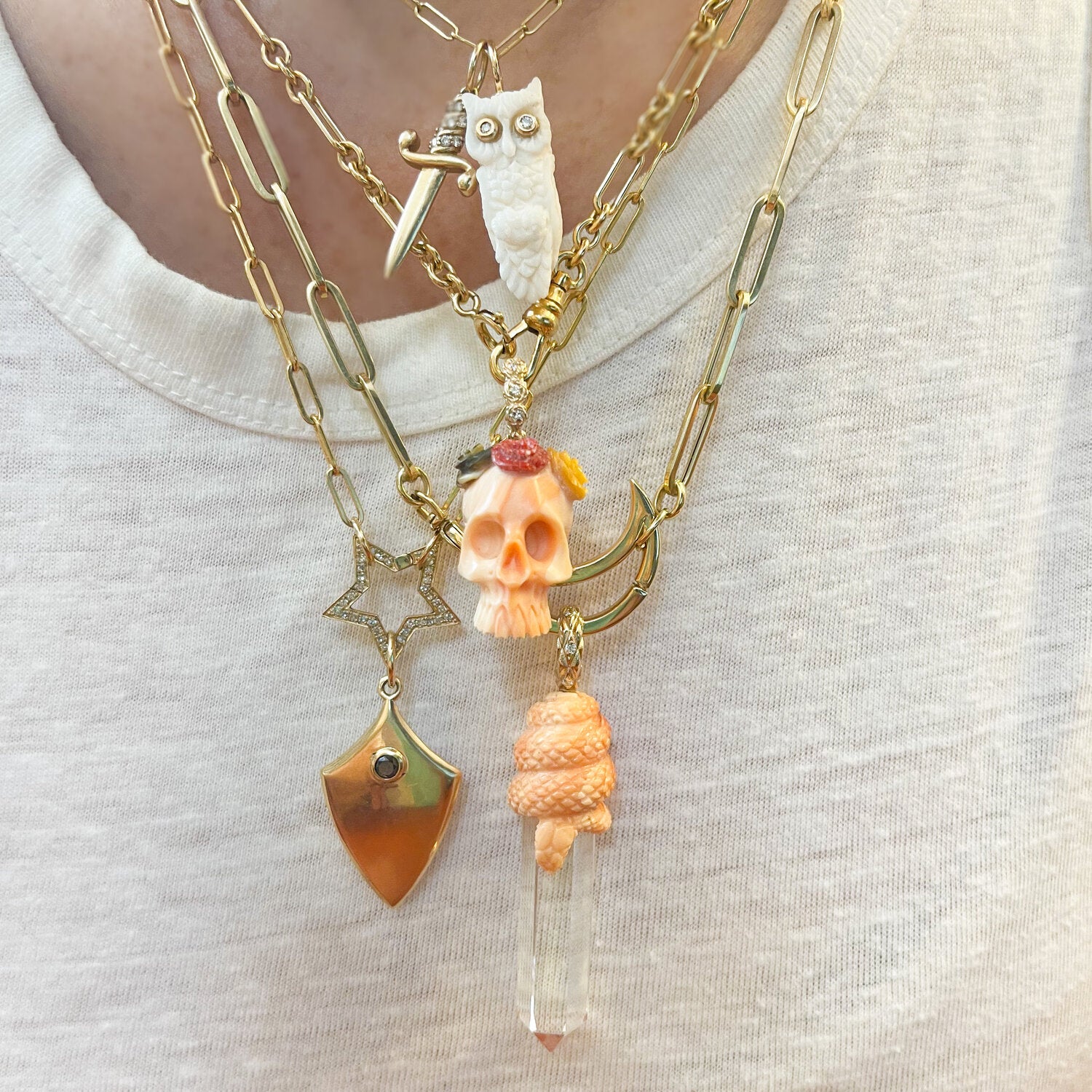 Clear crystal with light orange snake coiled about its top with gold bail shown worn on chain with other Maura Green necklaces around it