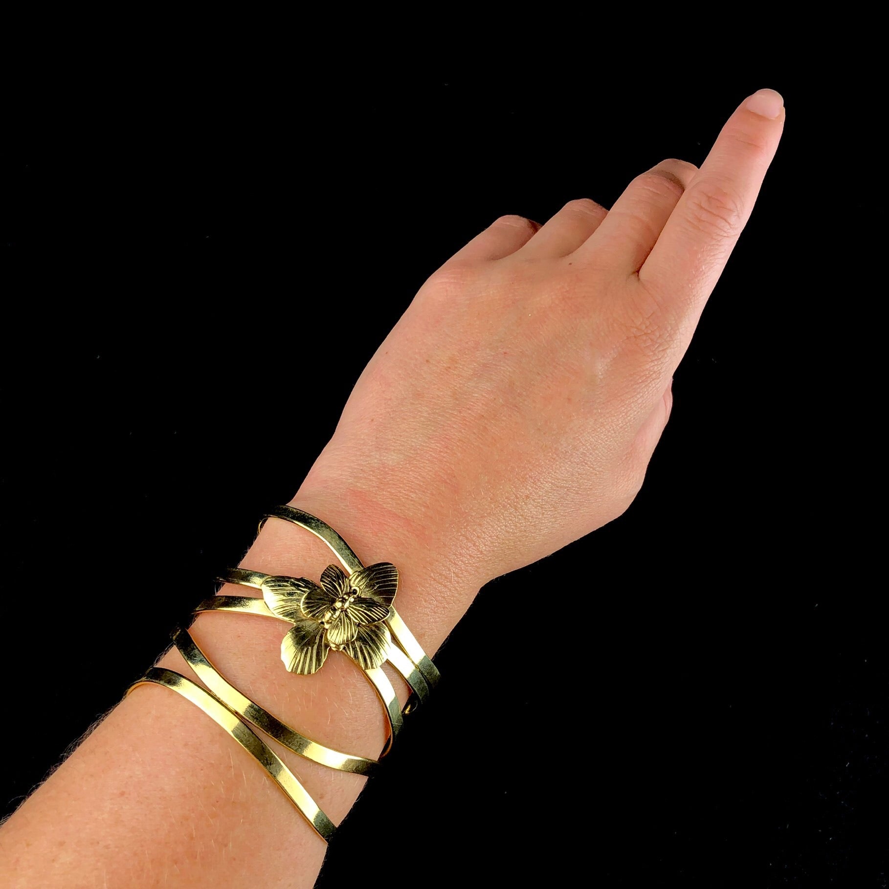 Golden metal ribbons wrap around the wrist and arm of this cuff with a small cut out butterfly adorning it