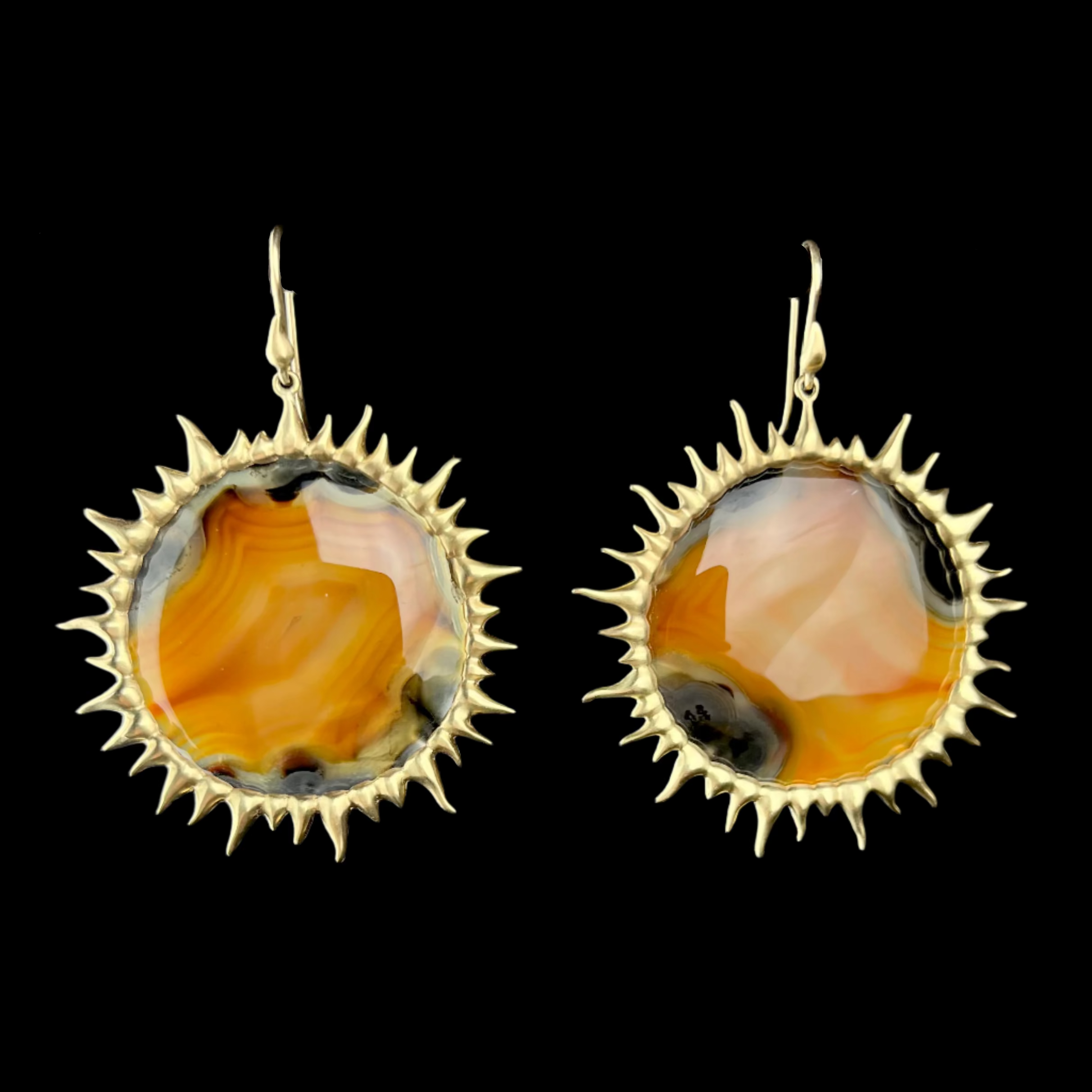 Gold-framed earrings with a central amber-colored stone on a black background
