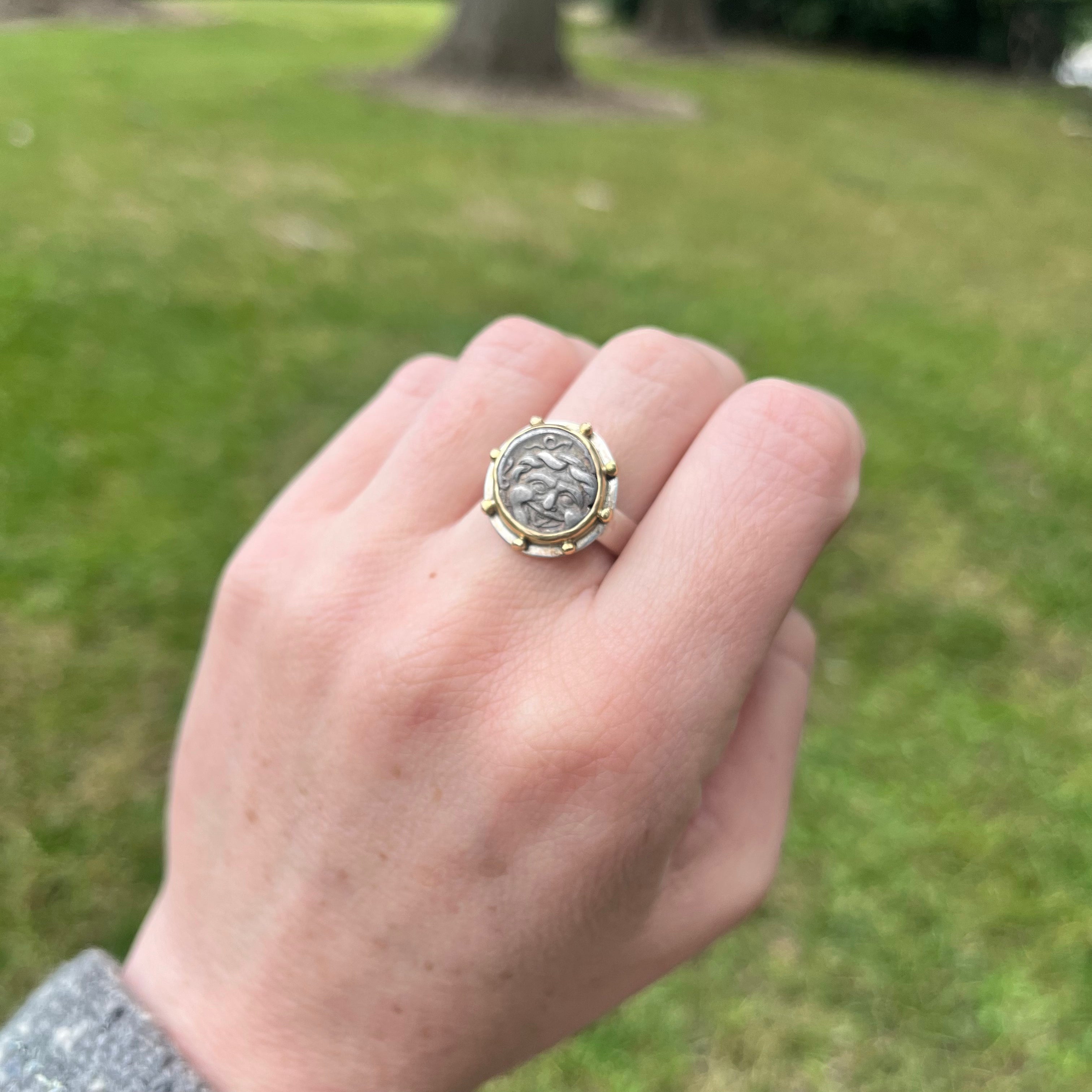 Hand wearing a ring with a coin design against a grassy background