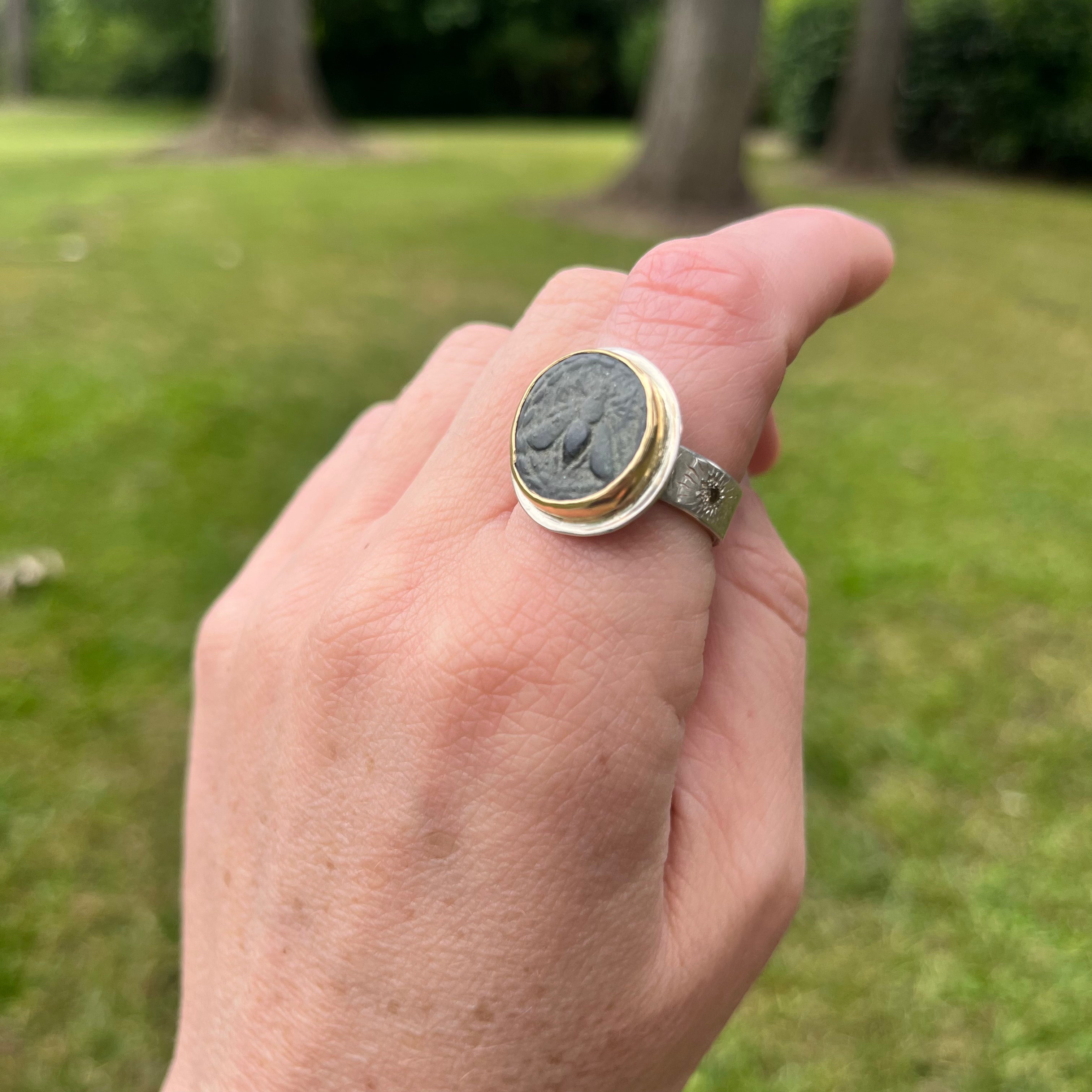 Hand wearing a ring with a green stone against a blurred outdoor background