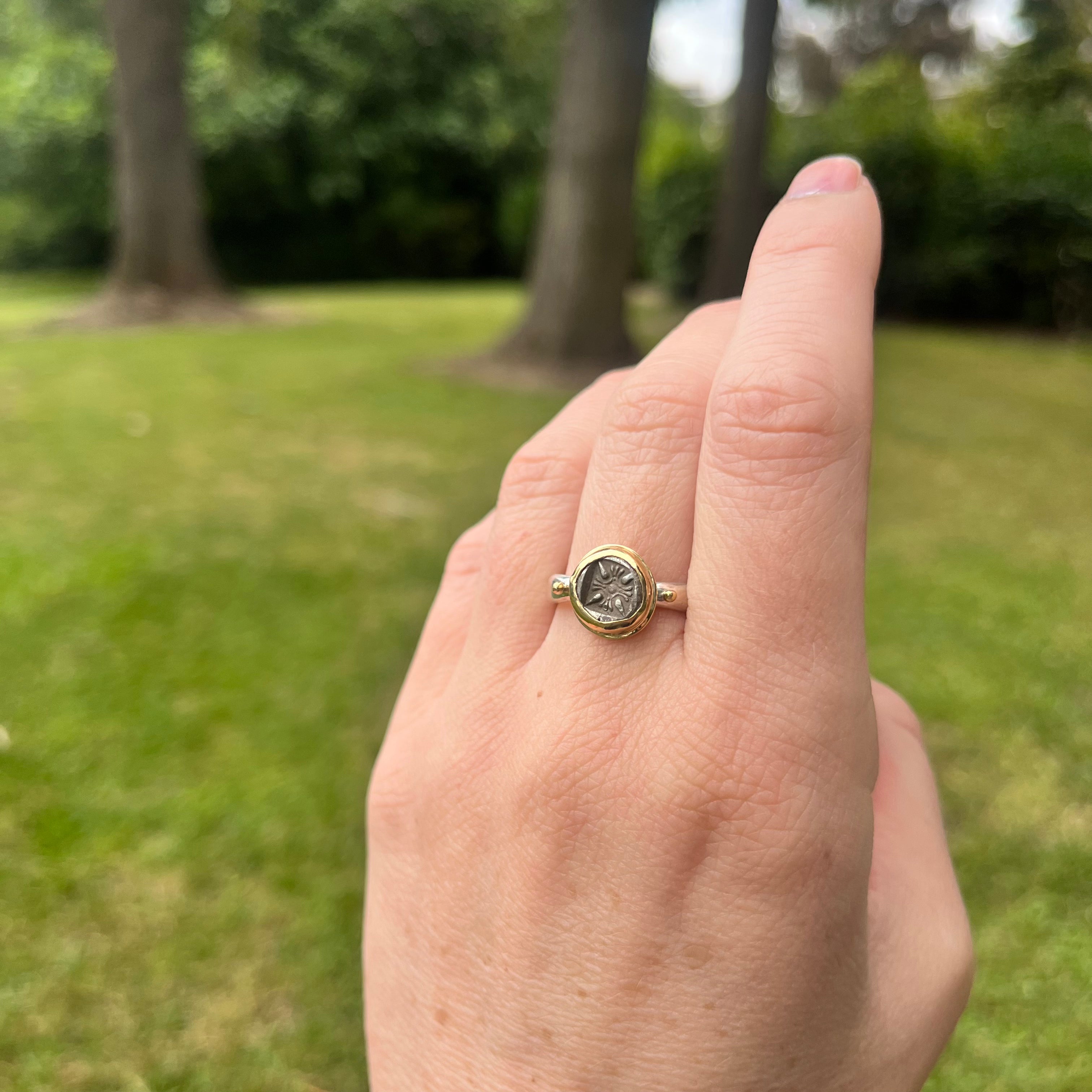 Hand wearing a ring with a green gemstone against a blurred outdoor background
