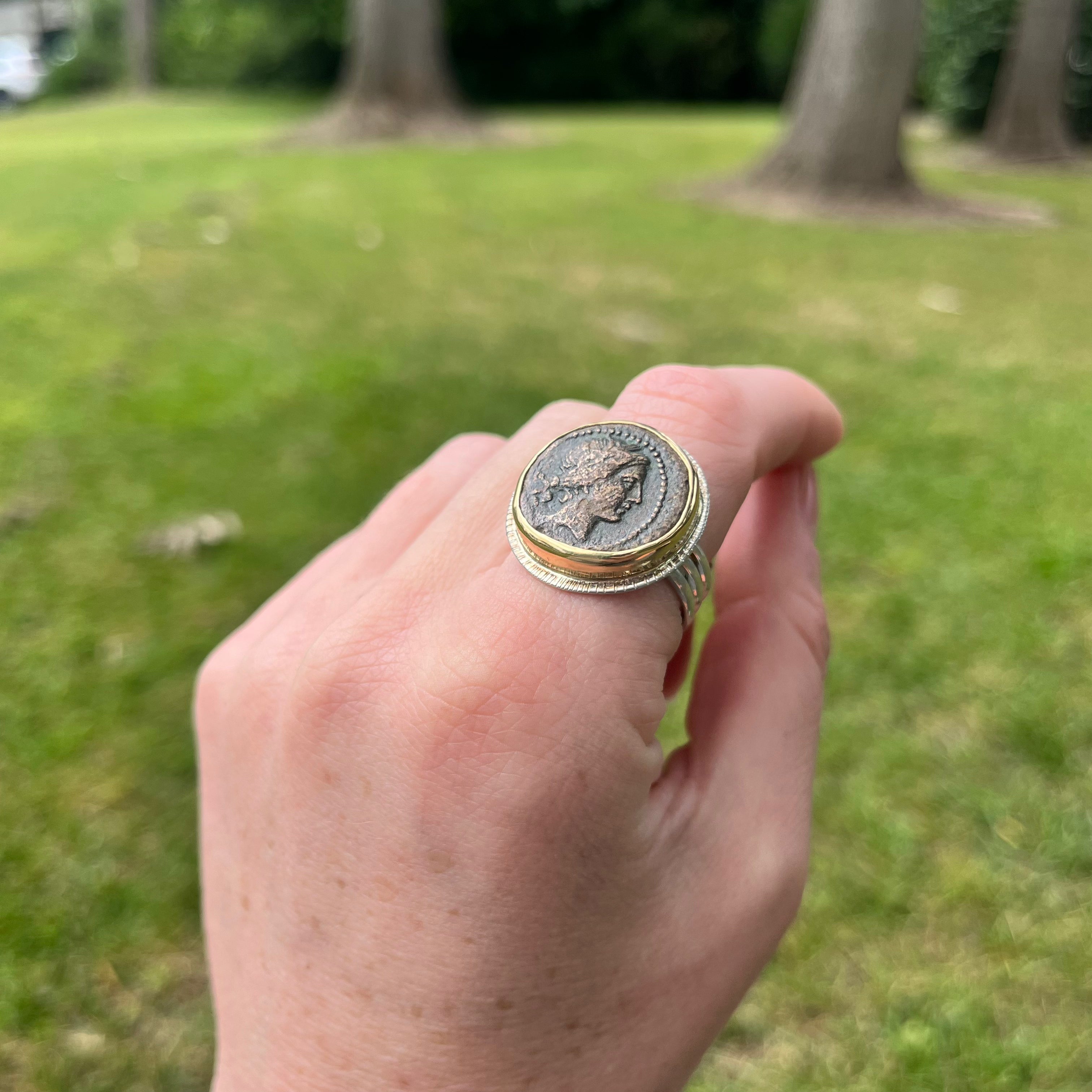 Hand wearing a ring with a coin design against a grassy background
