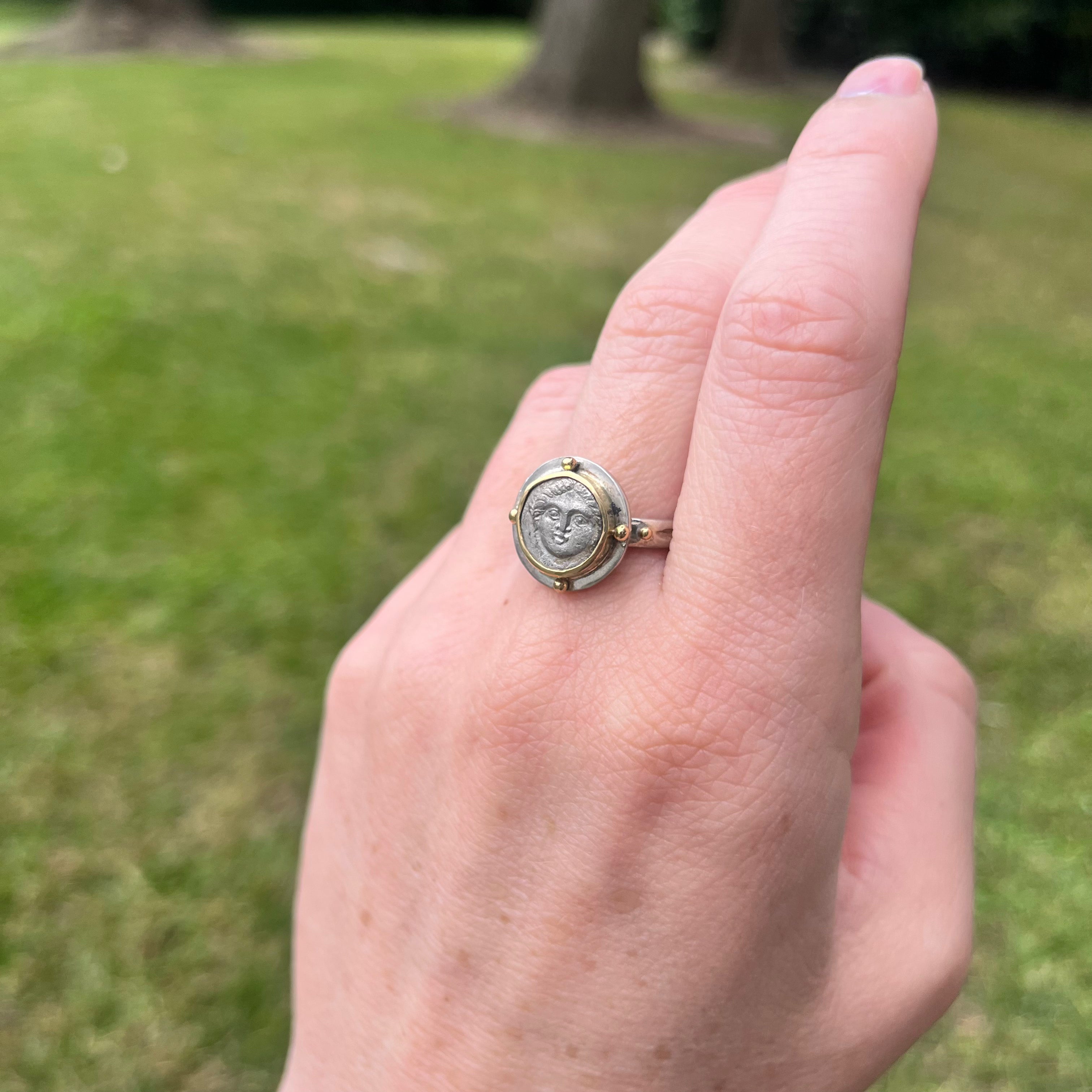 Hand wearing a decorative ring with a grassy background