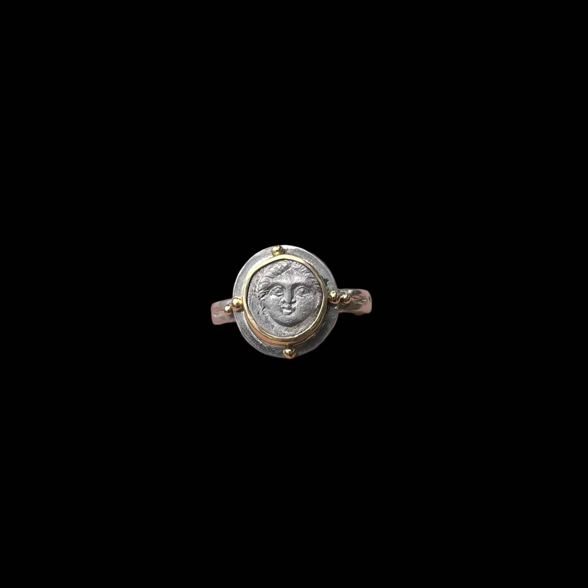 Hand wearing a decorative ring with a face design against a grassy background
