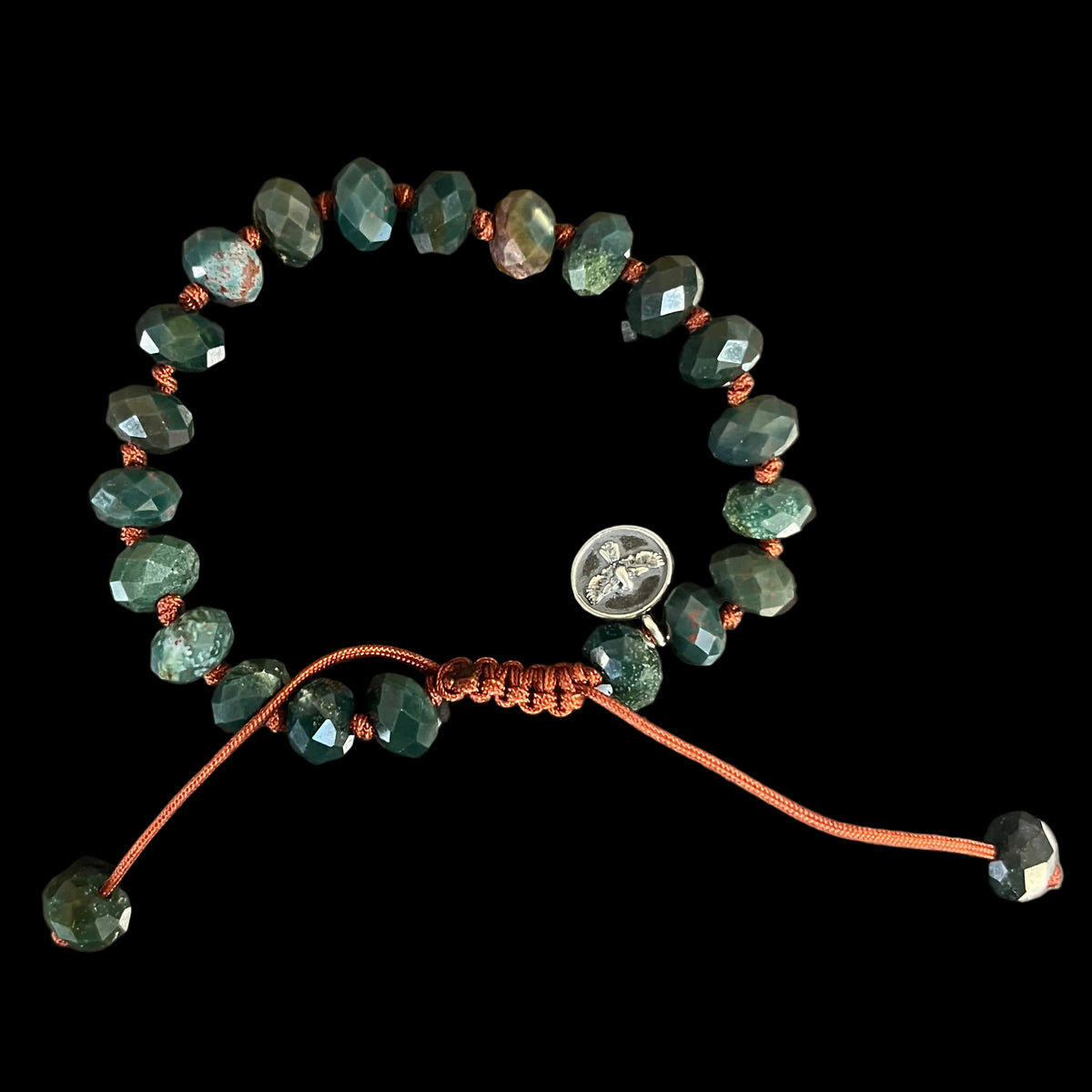 A beaded bracelet made of faceted dark green beads with small orange spacer beads, an orange adjustable cord, and a small round silver charm, in black background.