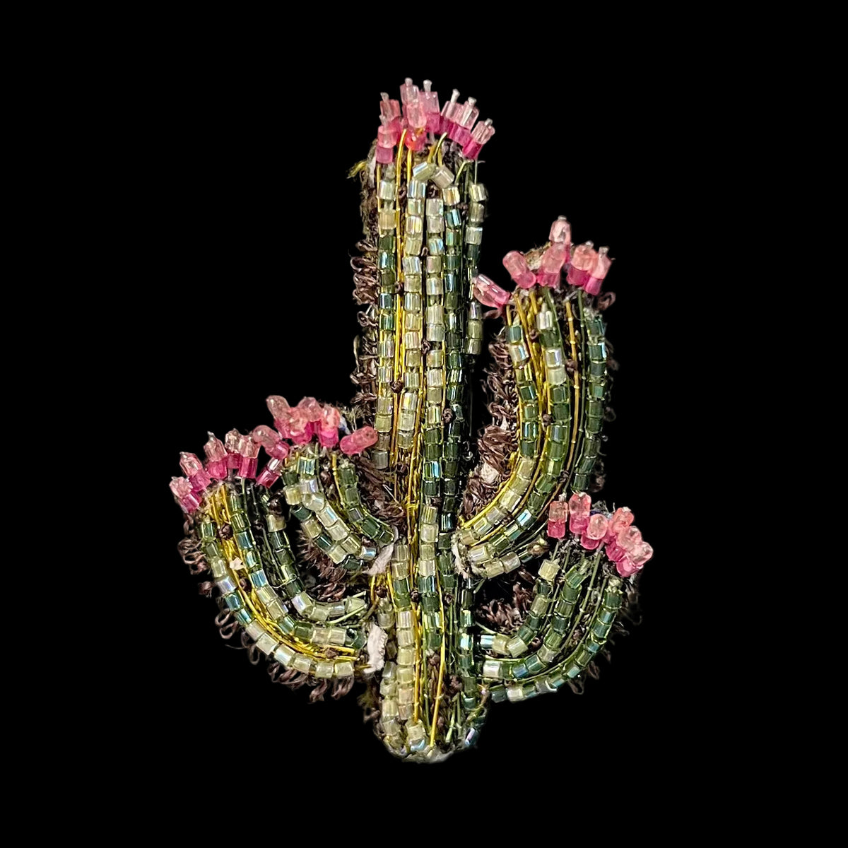 A handmade beaded cactus brooch featuring green and iridescent beads with pink faux flowers, displayed against a solid black background.