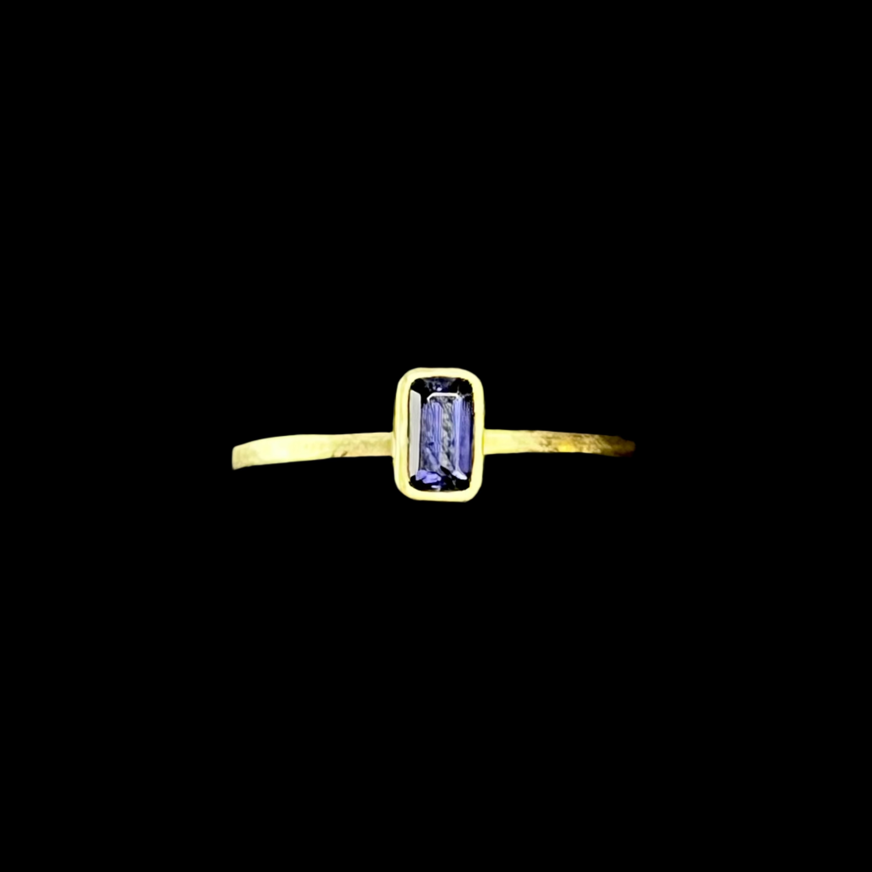 Gold ring with a rectangular purple gemstone on a dark background