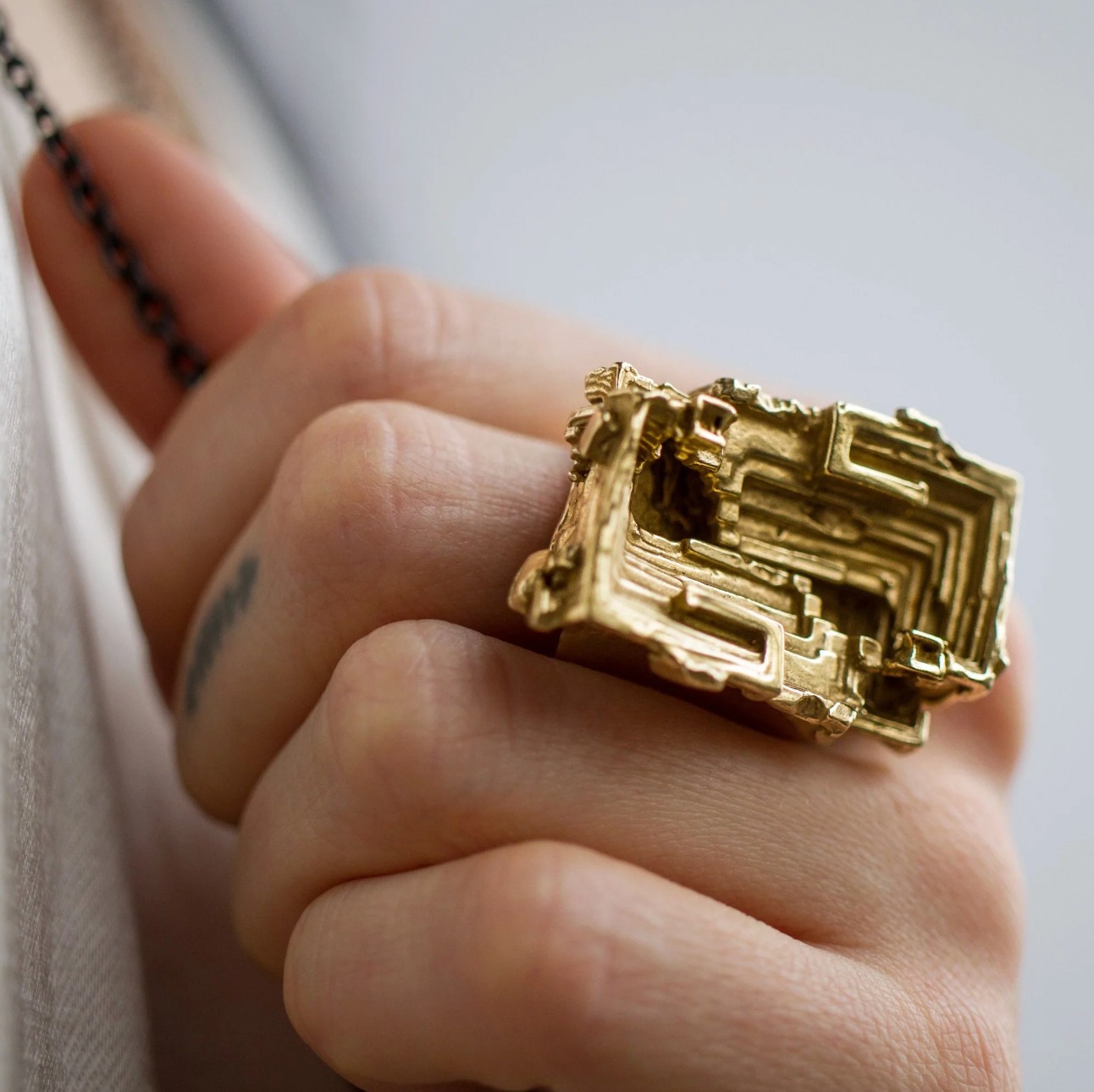 Gold ring with geometric design on a person's finger against a neutral background