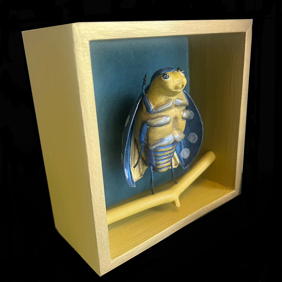 Beetle sculpture in wooden box painted in blues, yellows. 
