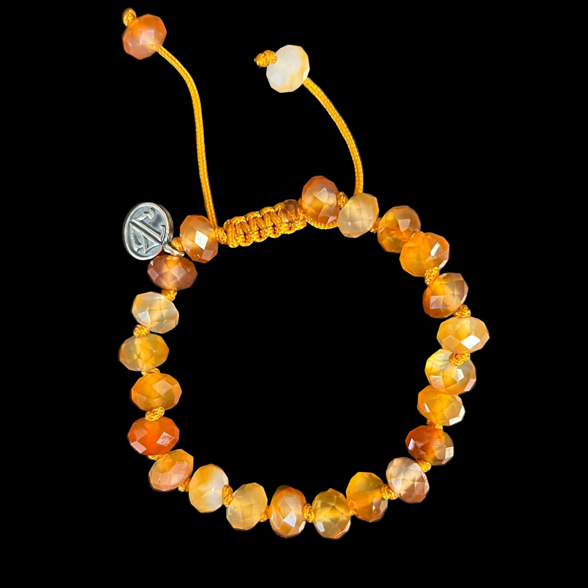 A beaded bracelet made of faceted amber-orange beads on a dark background, with an adjustable orange cord and a small silver-toned charm.
