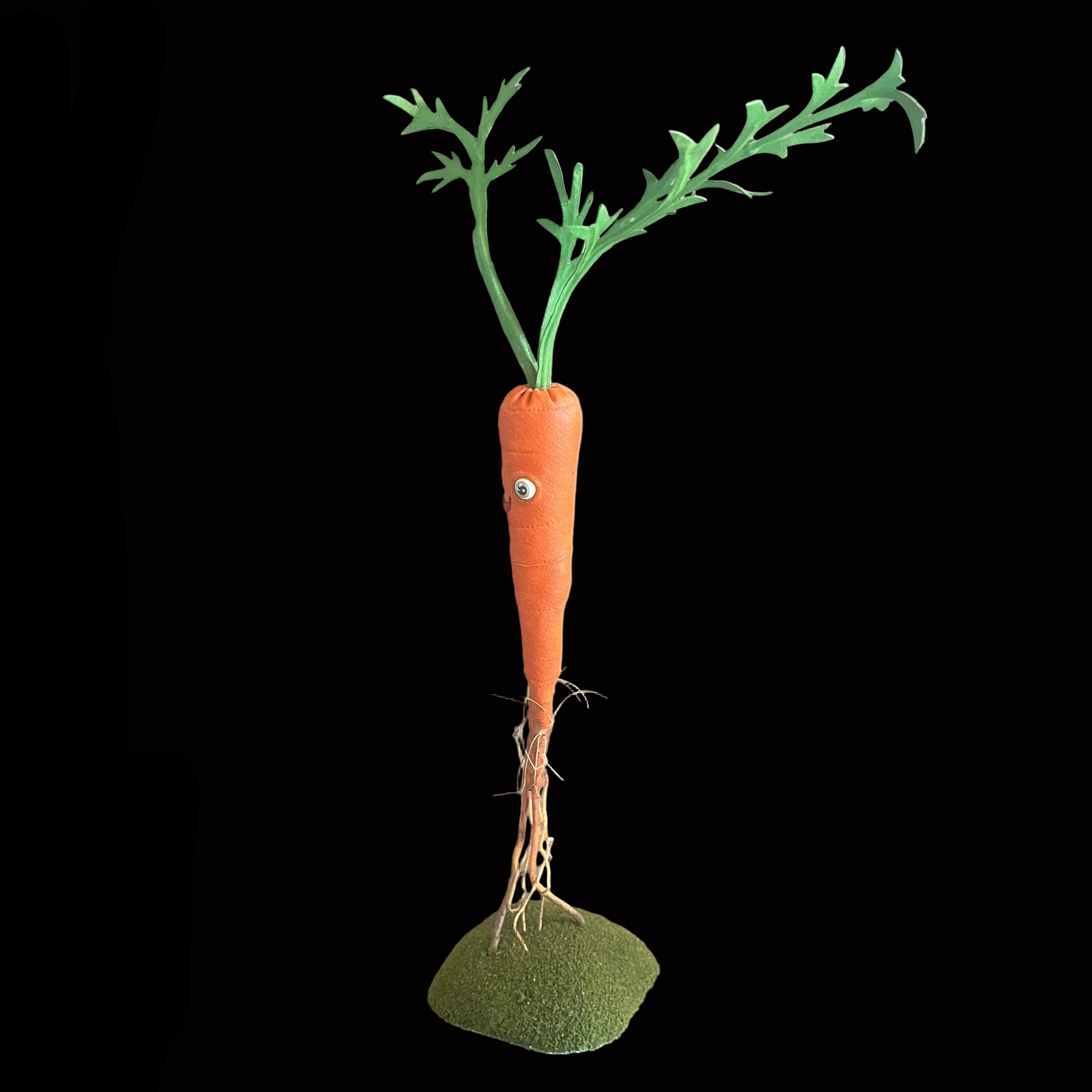 Whimsical carrot-shaped decorative figure standing on green turf base set against black background, side view.