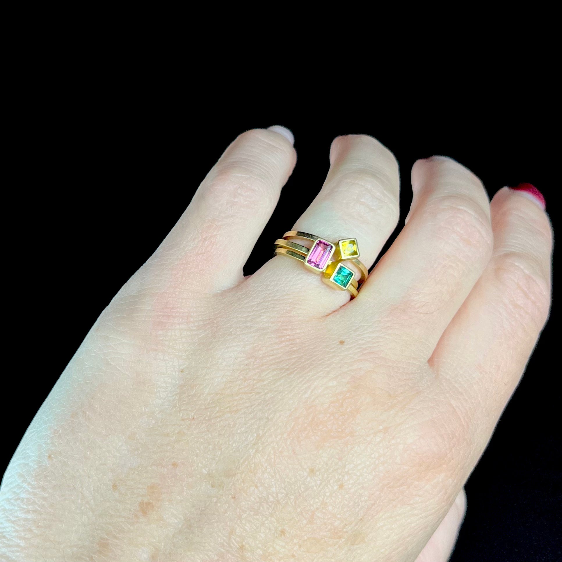 Hand wearing gold rings with colorful gemstones on a black background