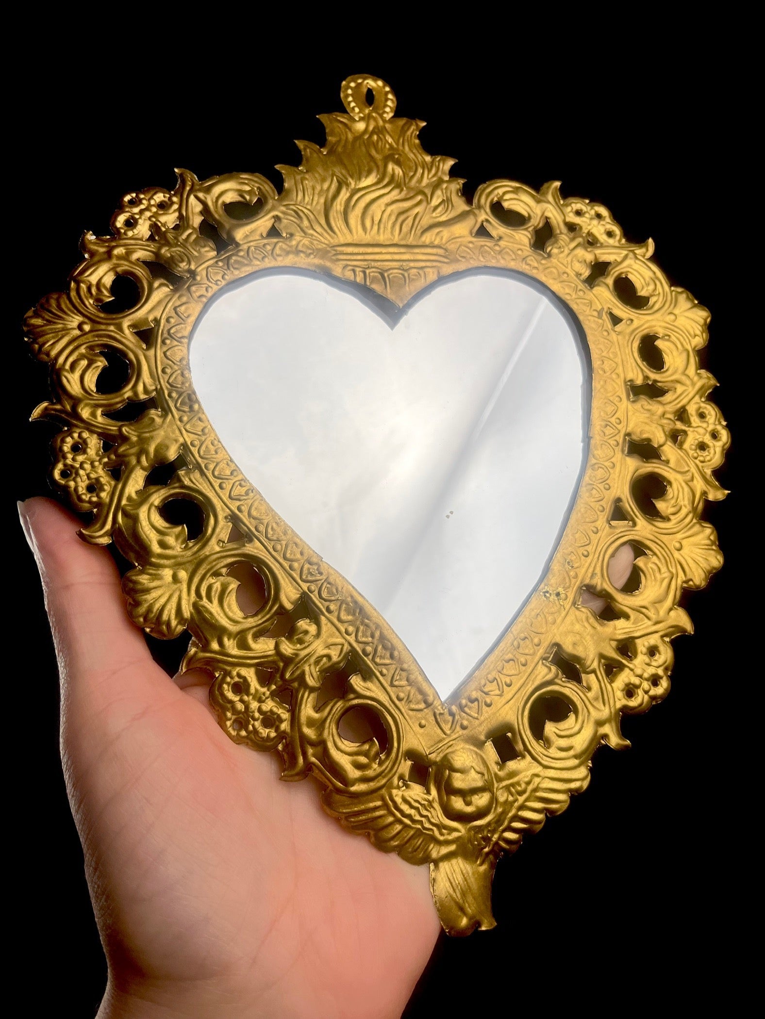 Decorative gold heart-shaped mirror held by a hand against a black background