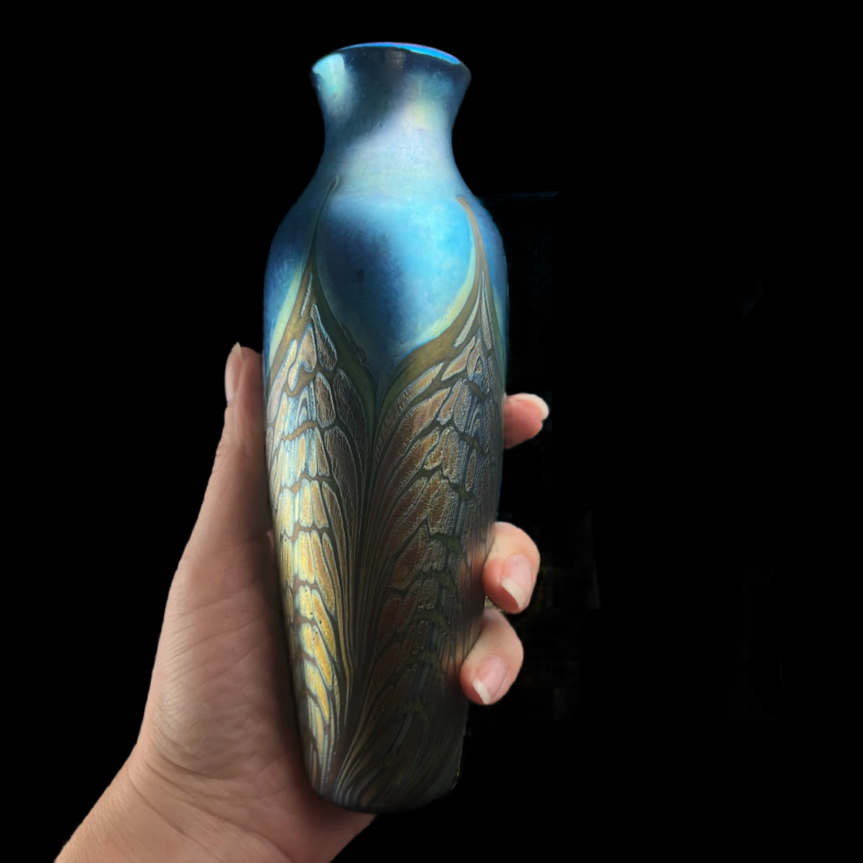 Hand holding a decorative vase with two other vases in the background on a dark background