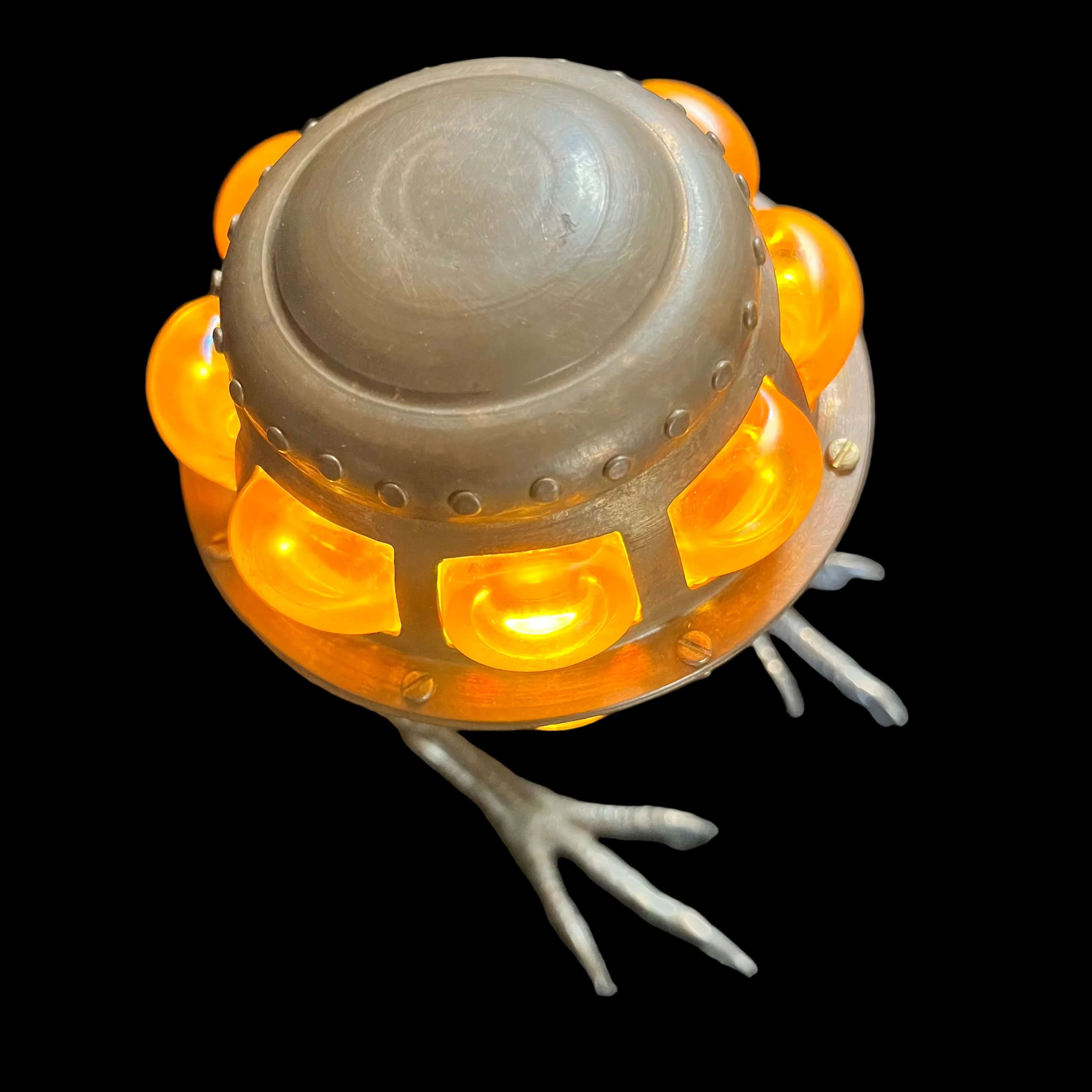 Metallic owl-shaped object with orange lights on a dark surface