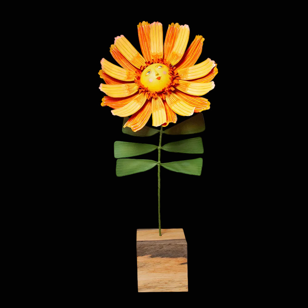 Bright yellow and orange flower sculpture with a smiling face in the center turned up petals standing a green stem with square wooden base. 