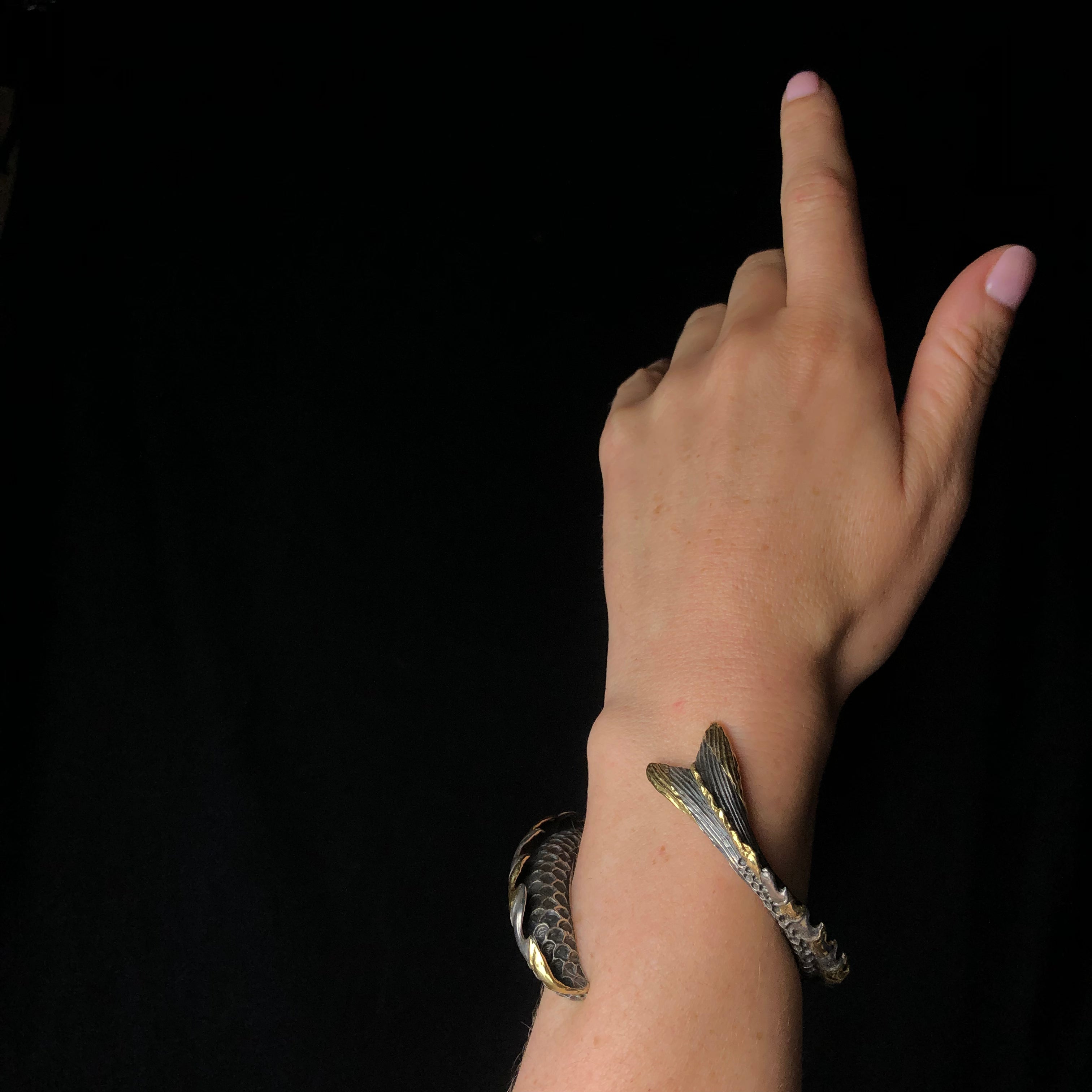 Silver bracelet resembling a fish tail wrapping around a wrist against a black background