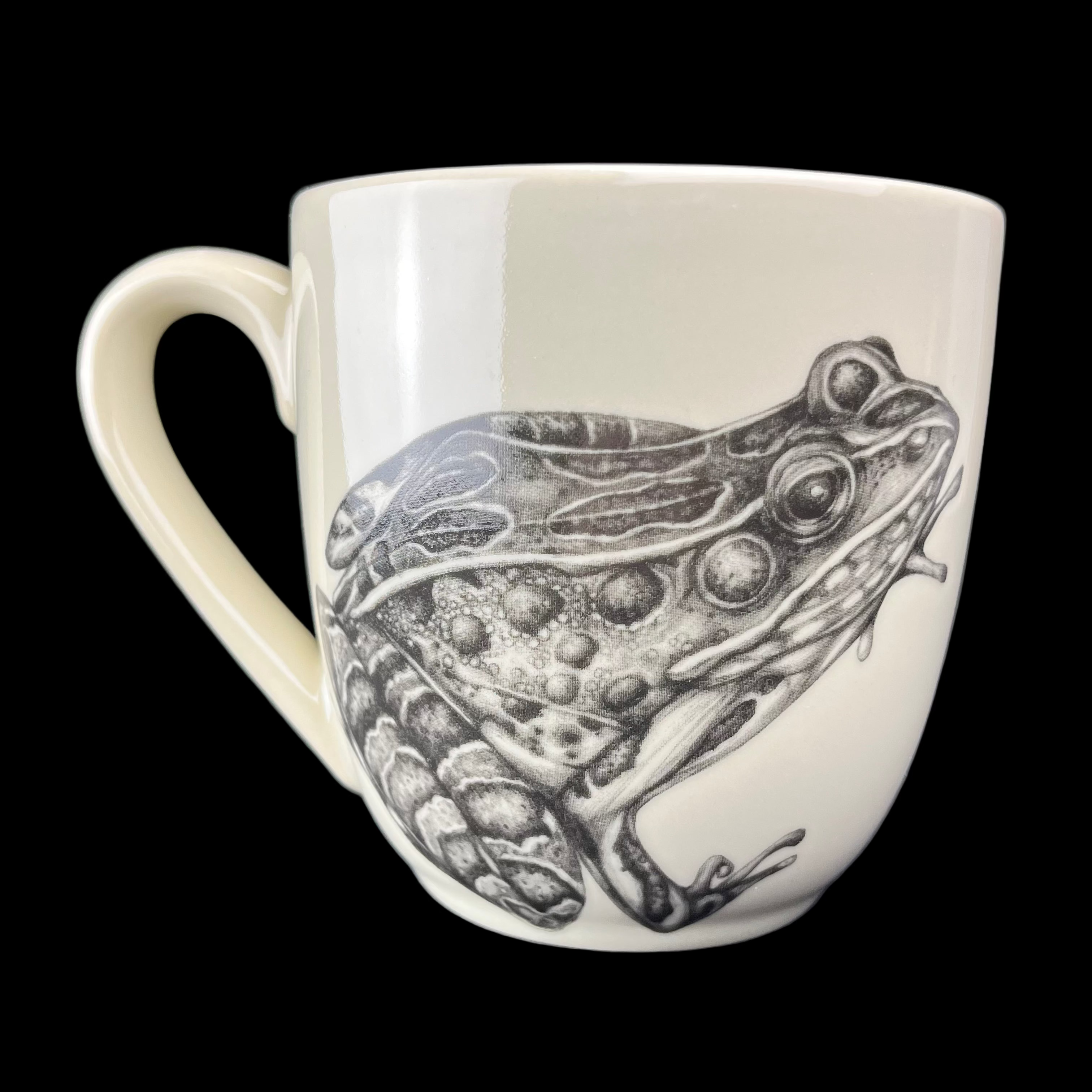 White mug with a black and white frog illustration on a dark background