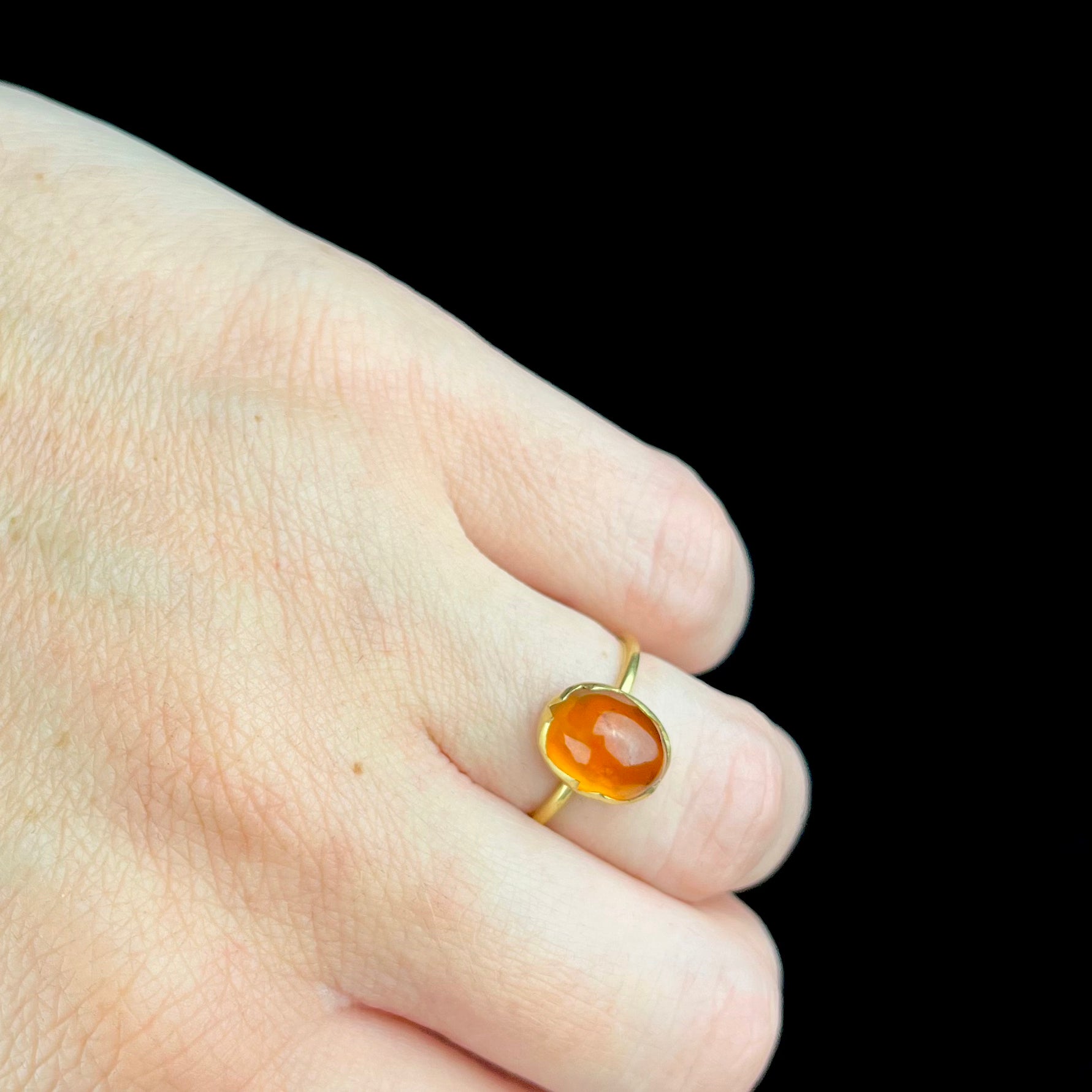 Gold ring with a red stone on a finger against a black background
