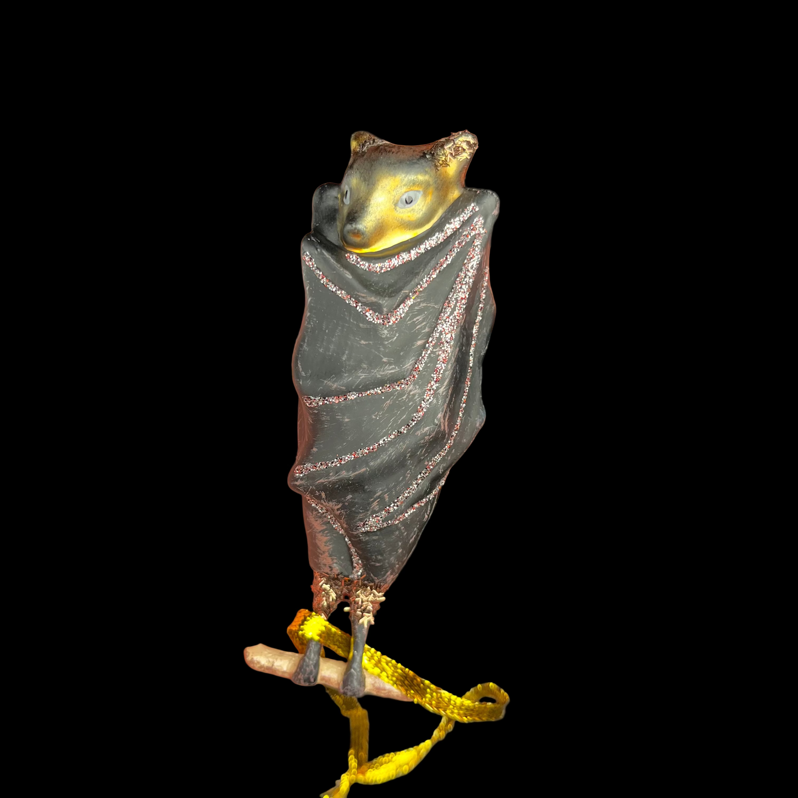 Hand holding a small decorative figurine of a creature wrapped in fabric with gold accents against a dark background