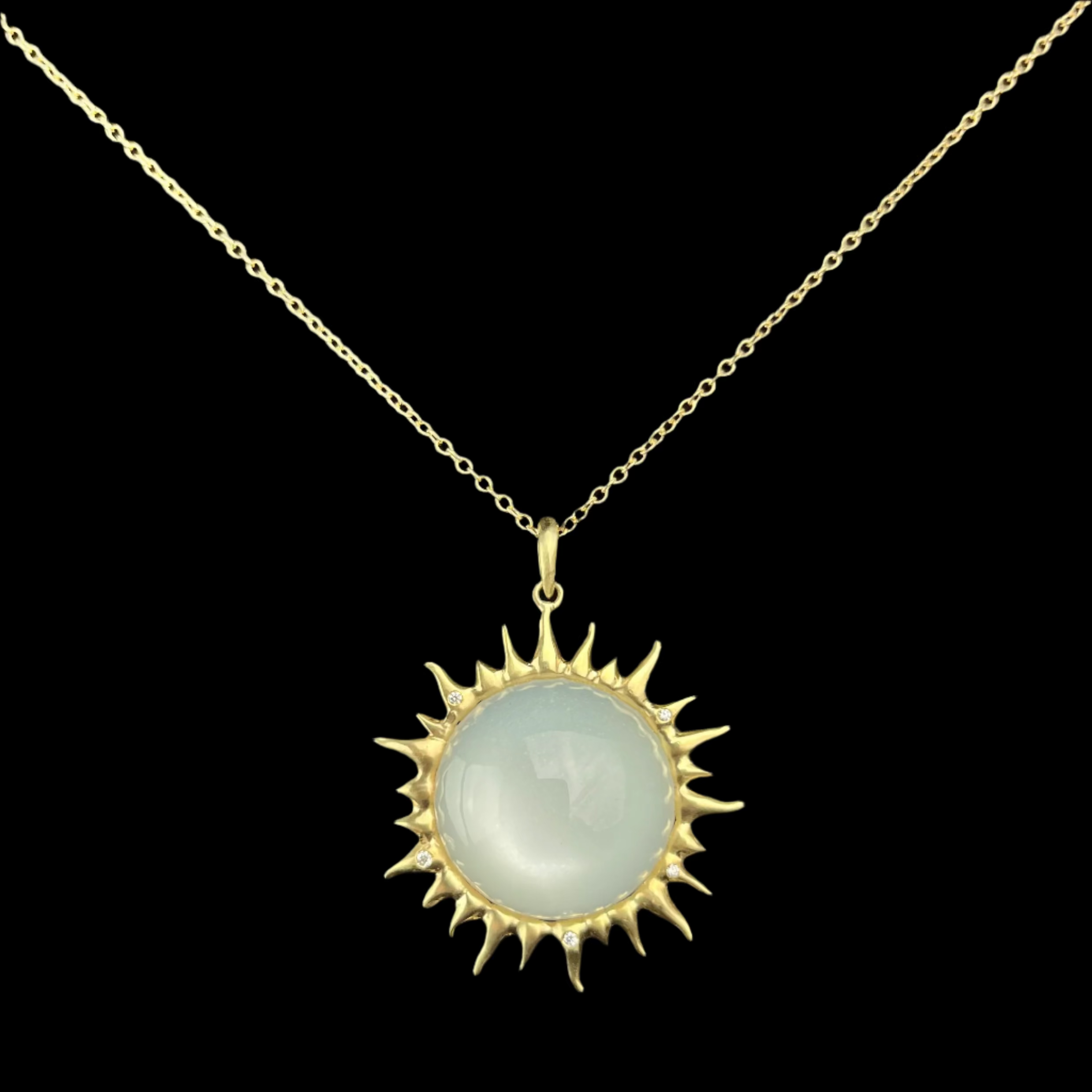 Gold necklace with a sun-shaped pendant featuring a white iridescent stone on a black background