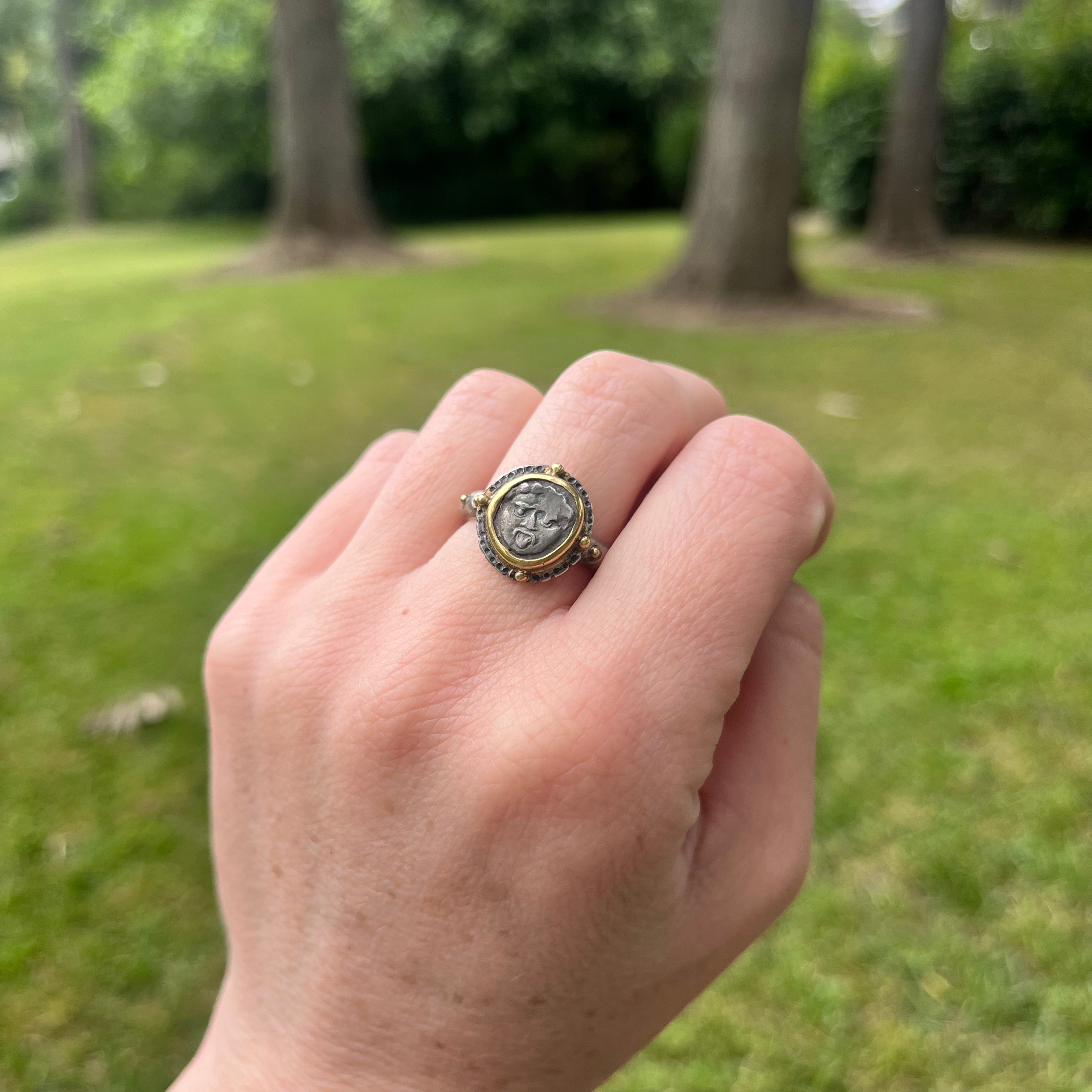 Hand wearing a decorative ring outdoors with greenery in the background