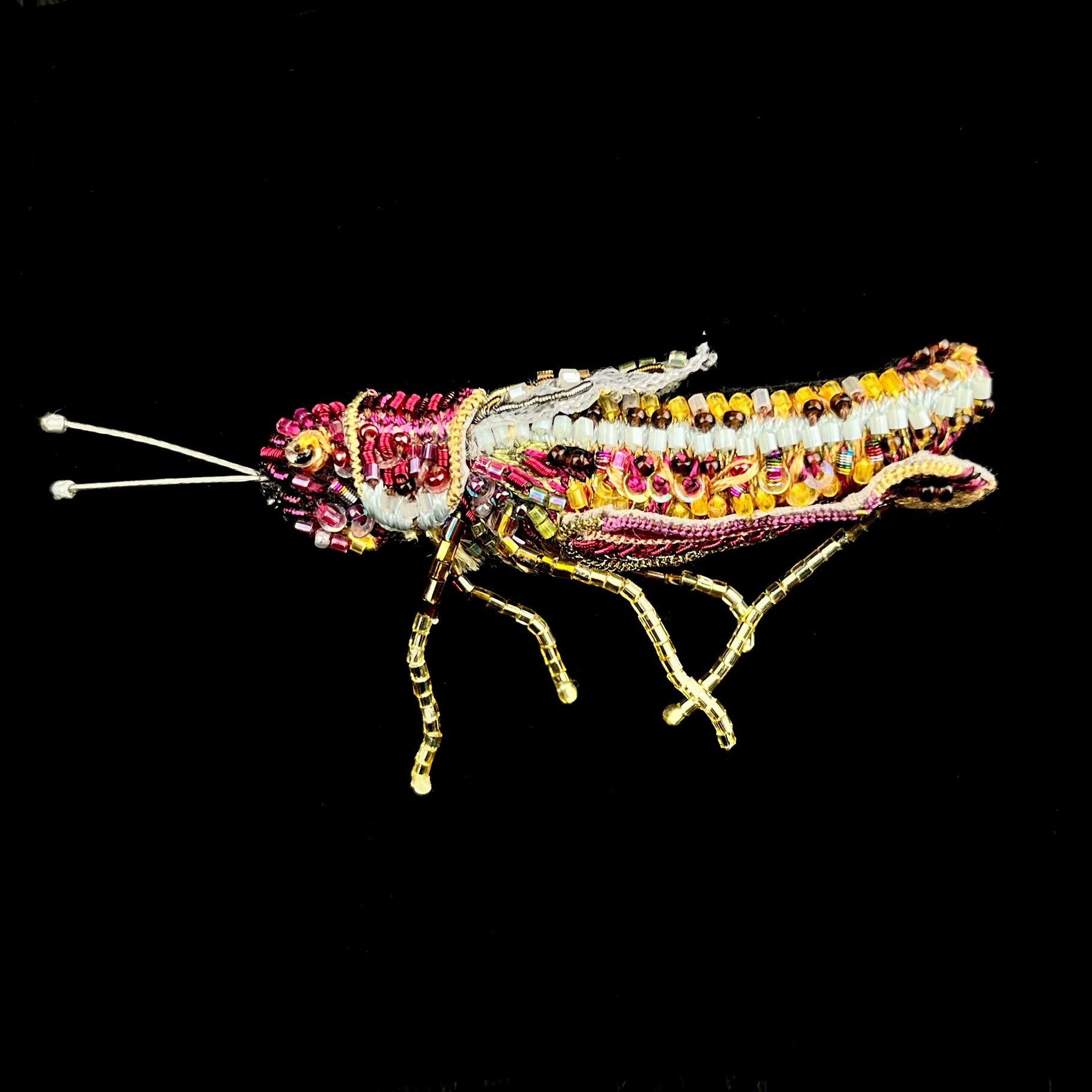 Grasshopper made of yellow, pink and brown thread with sparking glass bead accents and outstretched antenna and legs