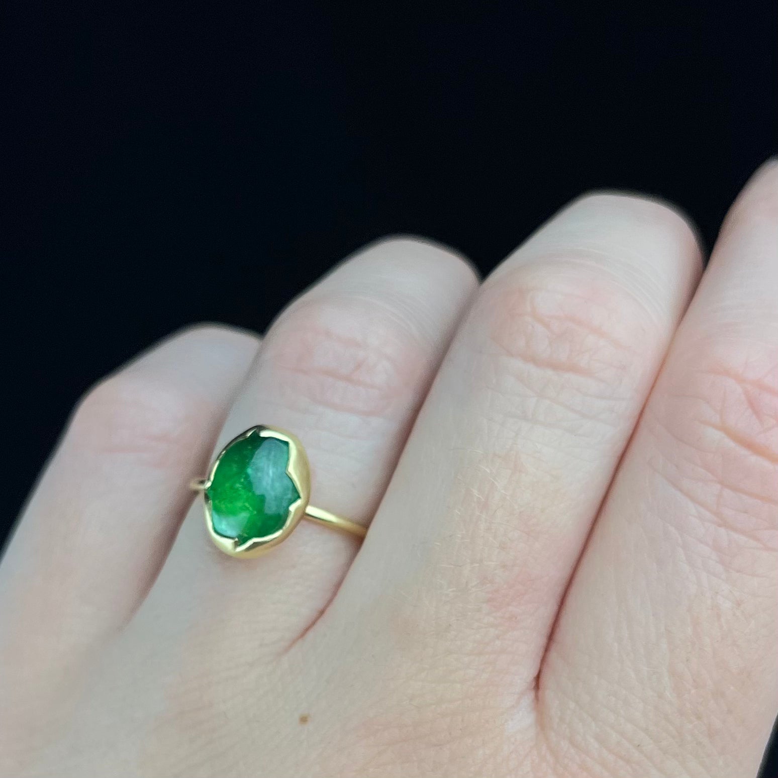 Gold ring with a green gemstone on a finger against a black background