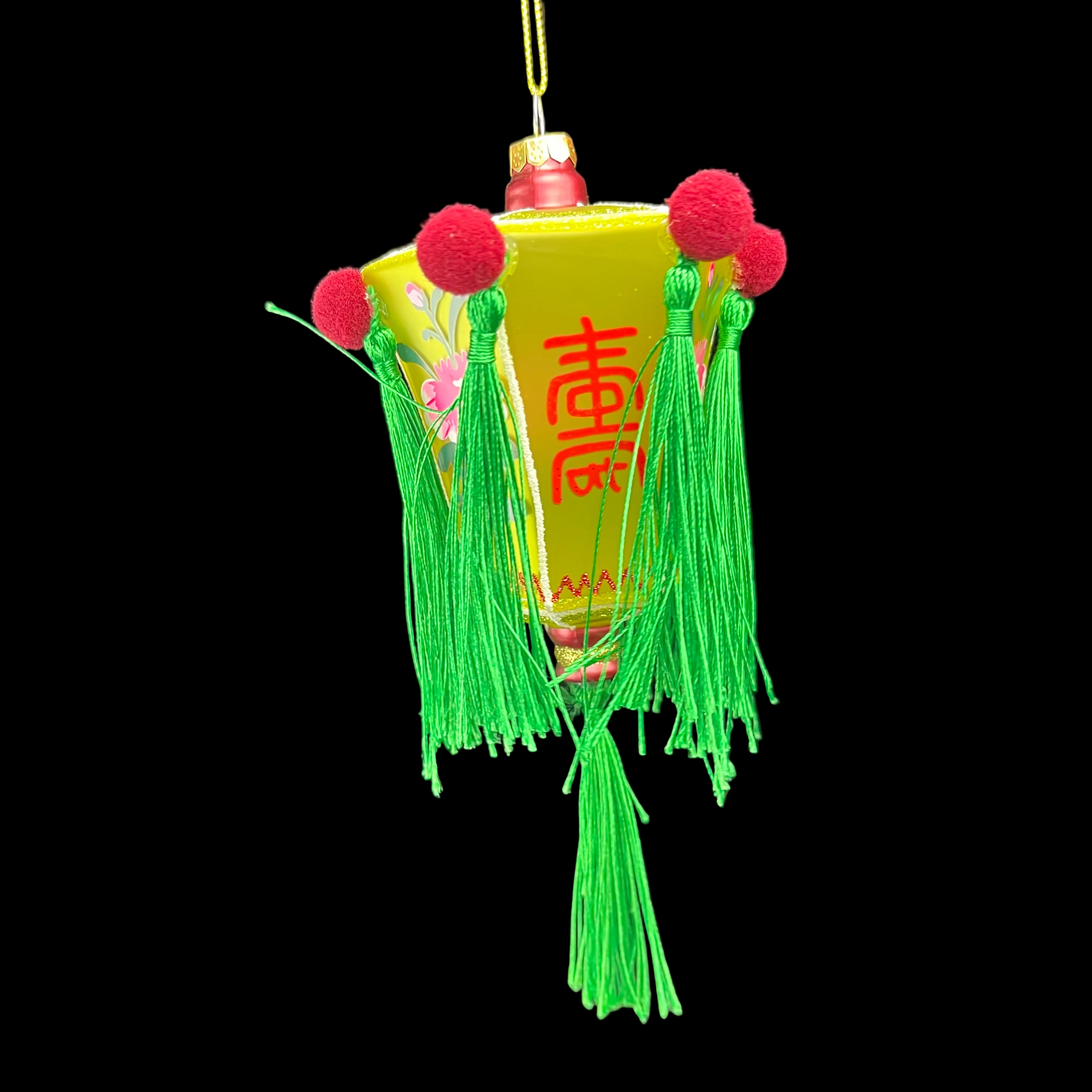 Decorative lantern with green tassels and red pom-poms on a black background