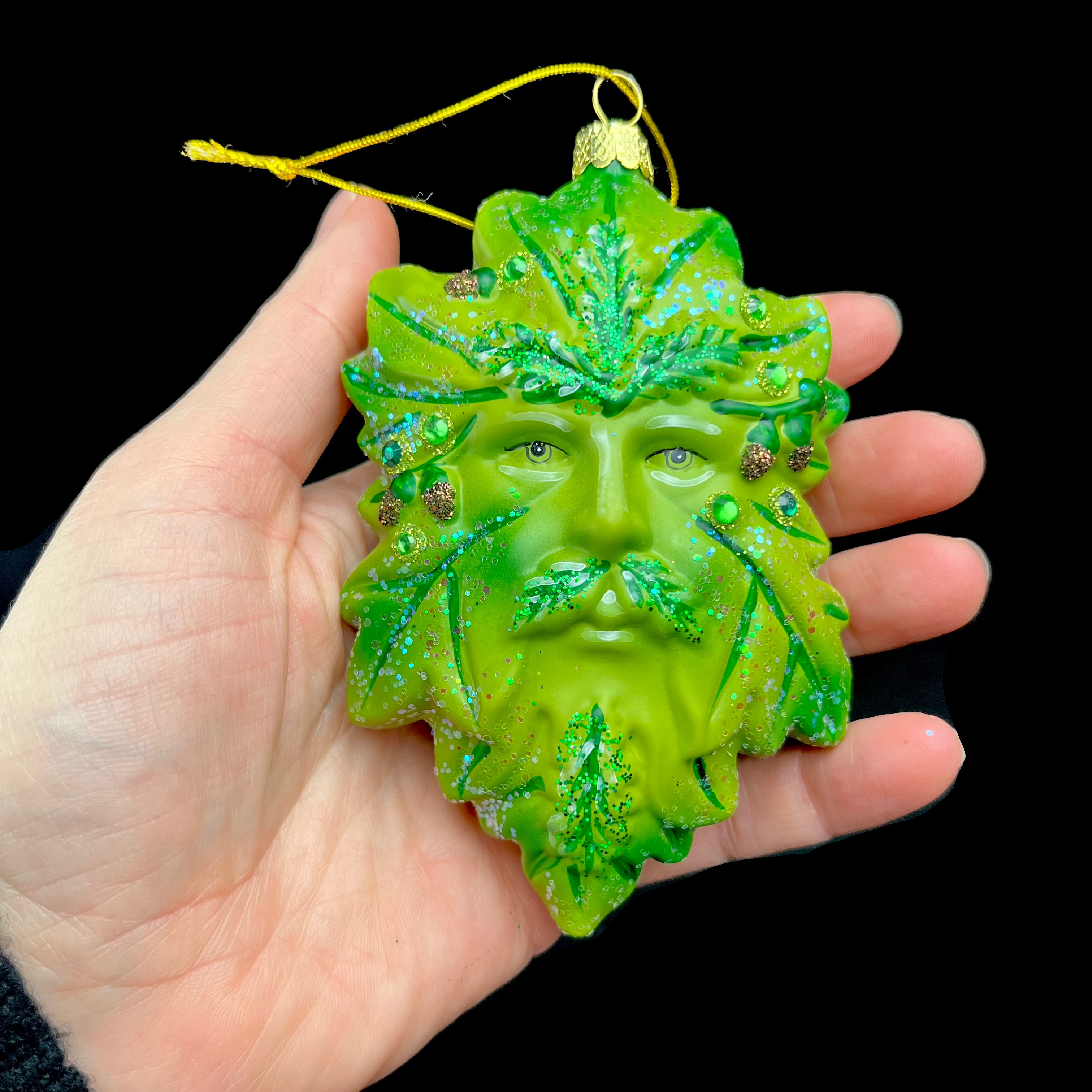 Green leaf-shaped ornament with face held in a hand against a black background