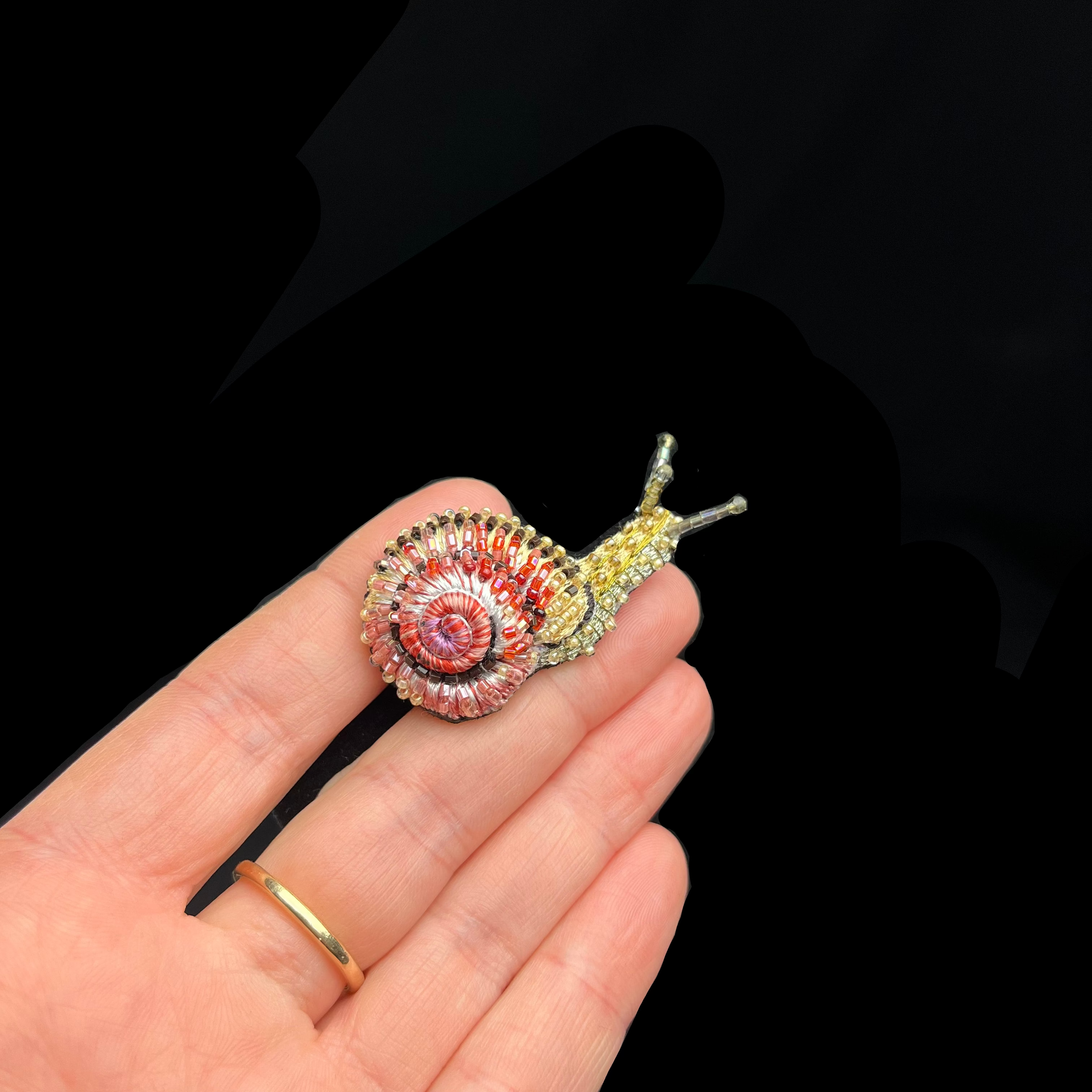 Colorful snail-shaped brooch on a hand with a black background