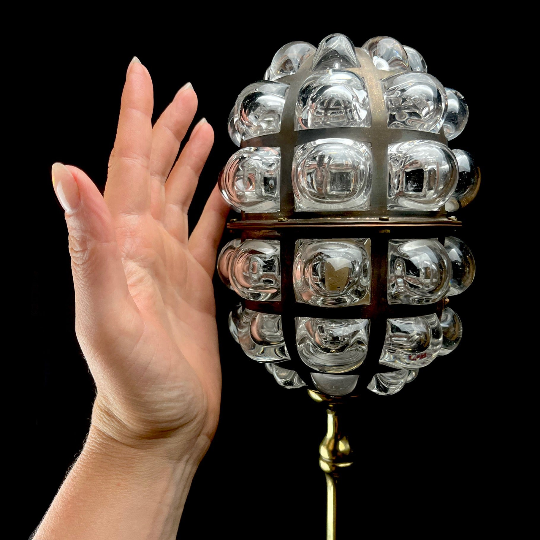 Decorative light fixture with a hand for scale on a black background