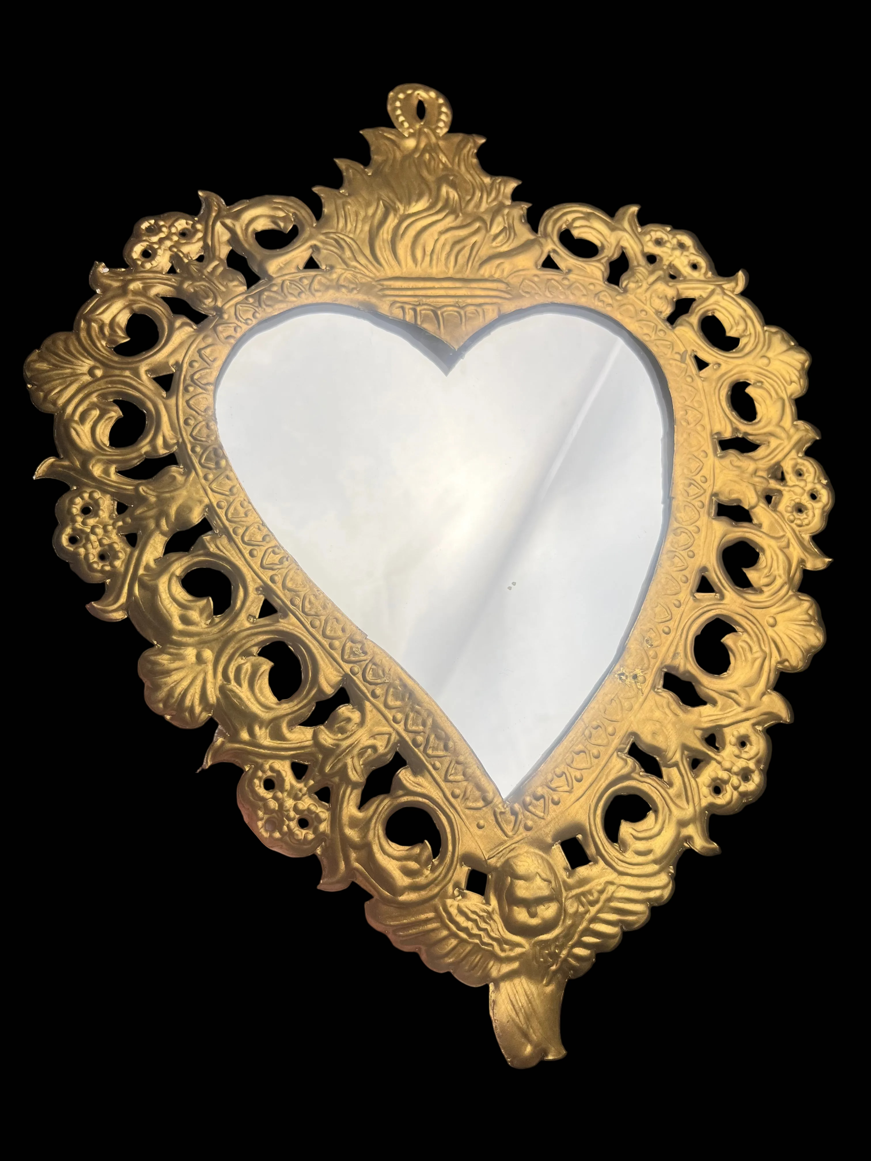 Decorative heart-shaped mirror with gold frame held by a hand against a dark background