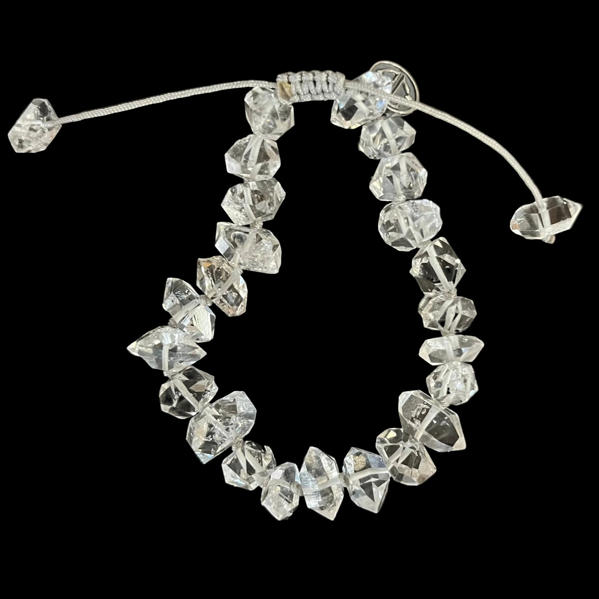 A clear faceted crystal bead bracelet with an adjustable cord closure, displayed on a dark, scratched surface.