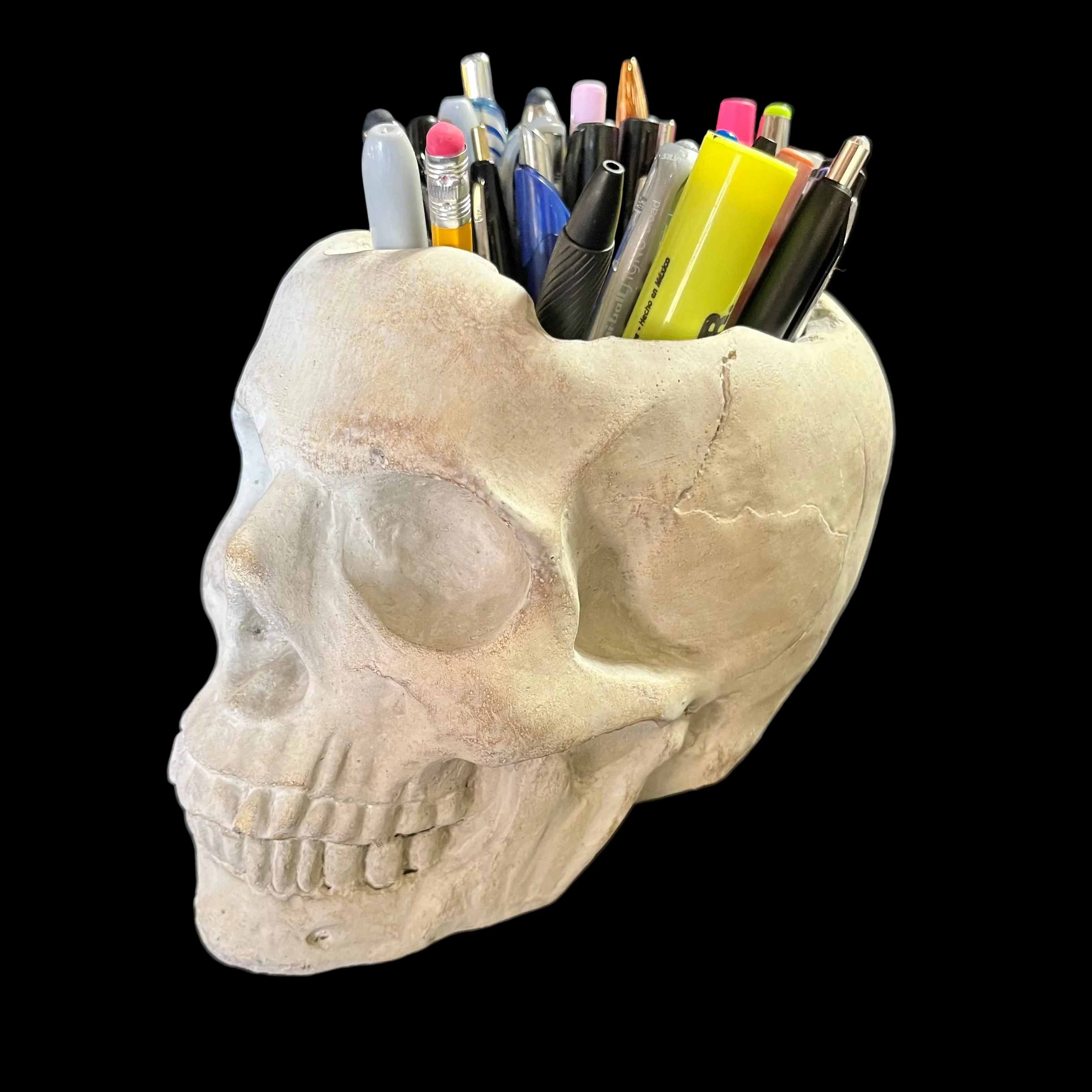 Skull-shaped pen holder with stationery items on a dark surface