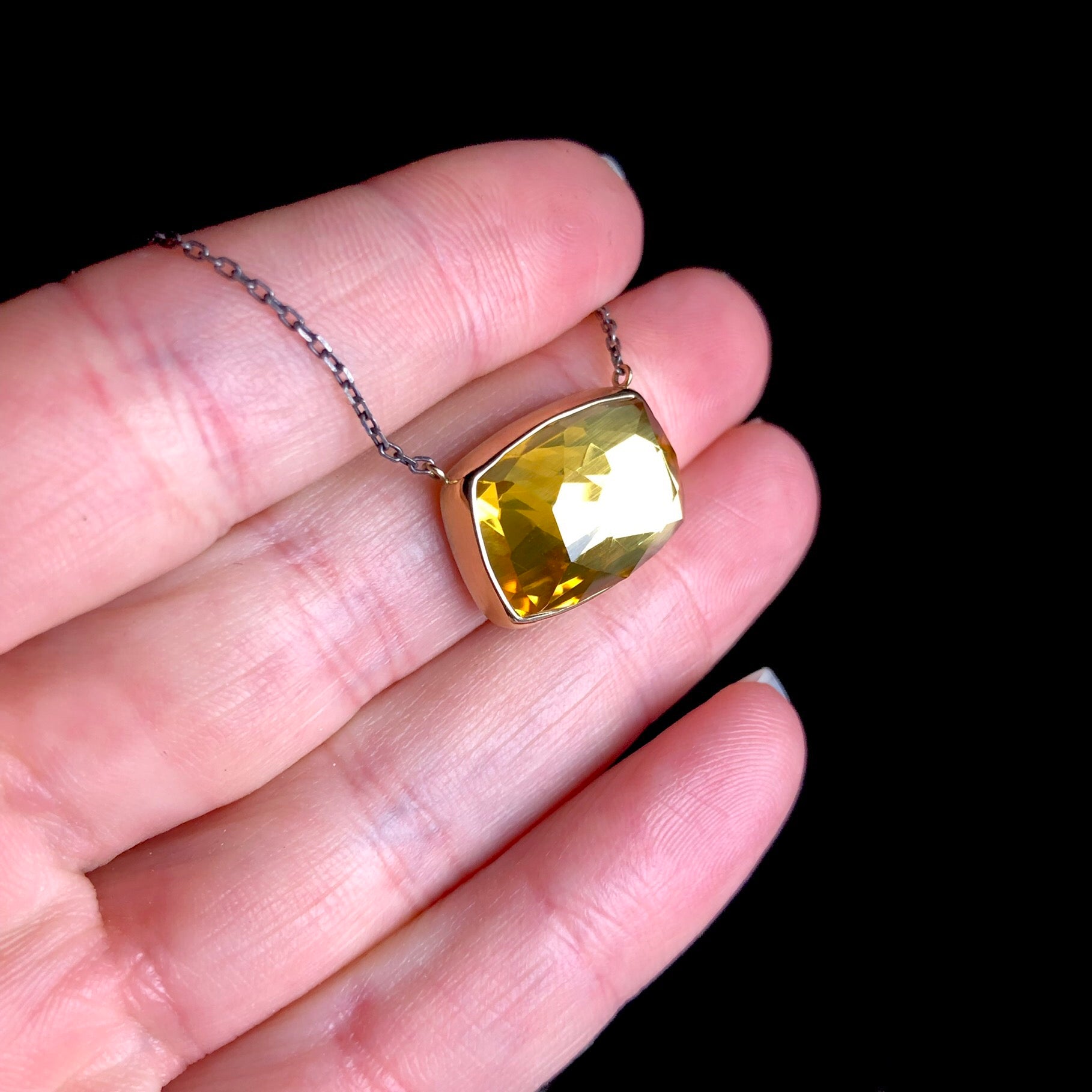 Yellow stone set in gold on blackened silver chain shown in hand