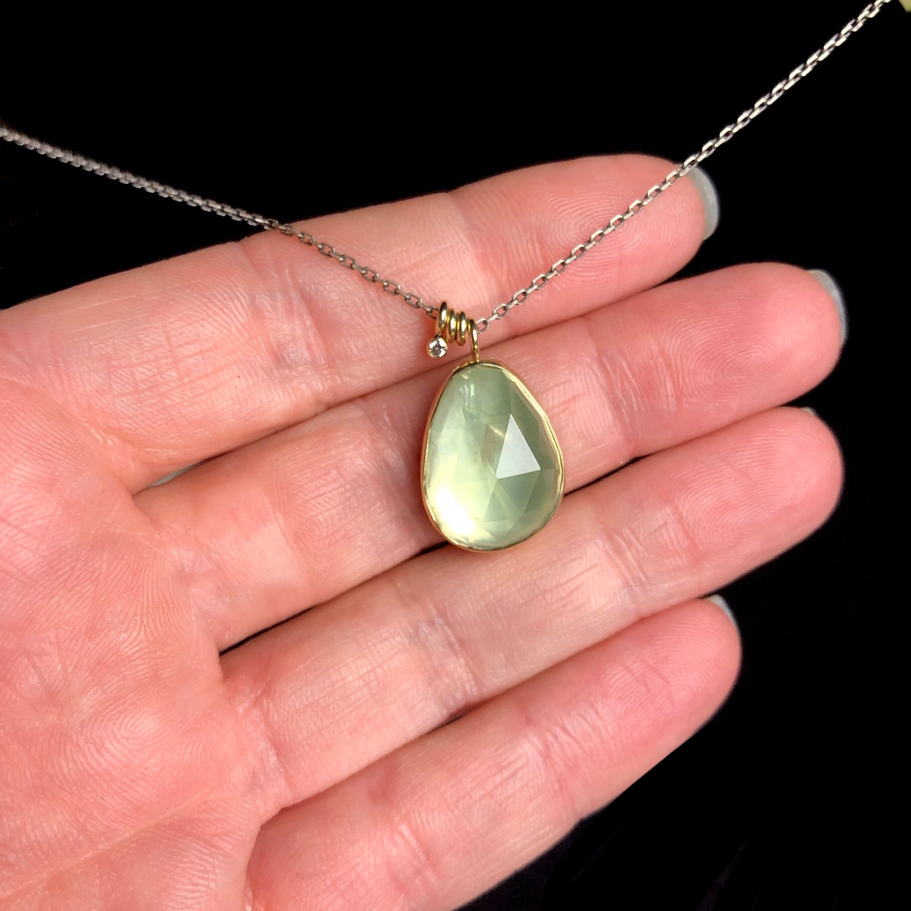 Light green teardrop shaped stone with gold setting on blackened silver chain shown in hand
