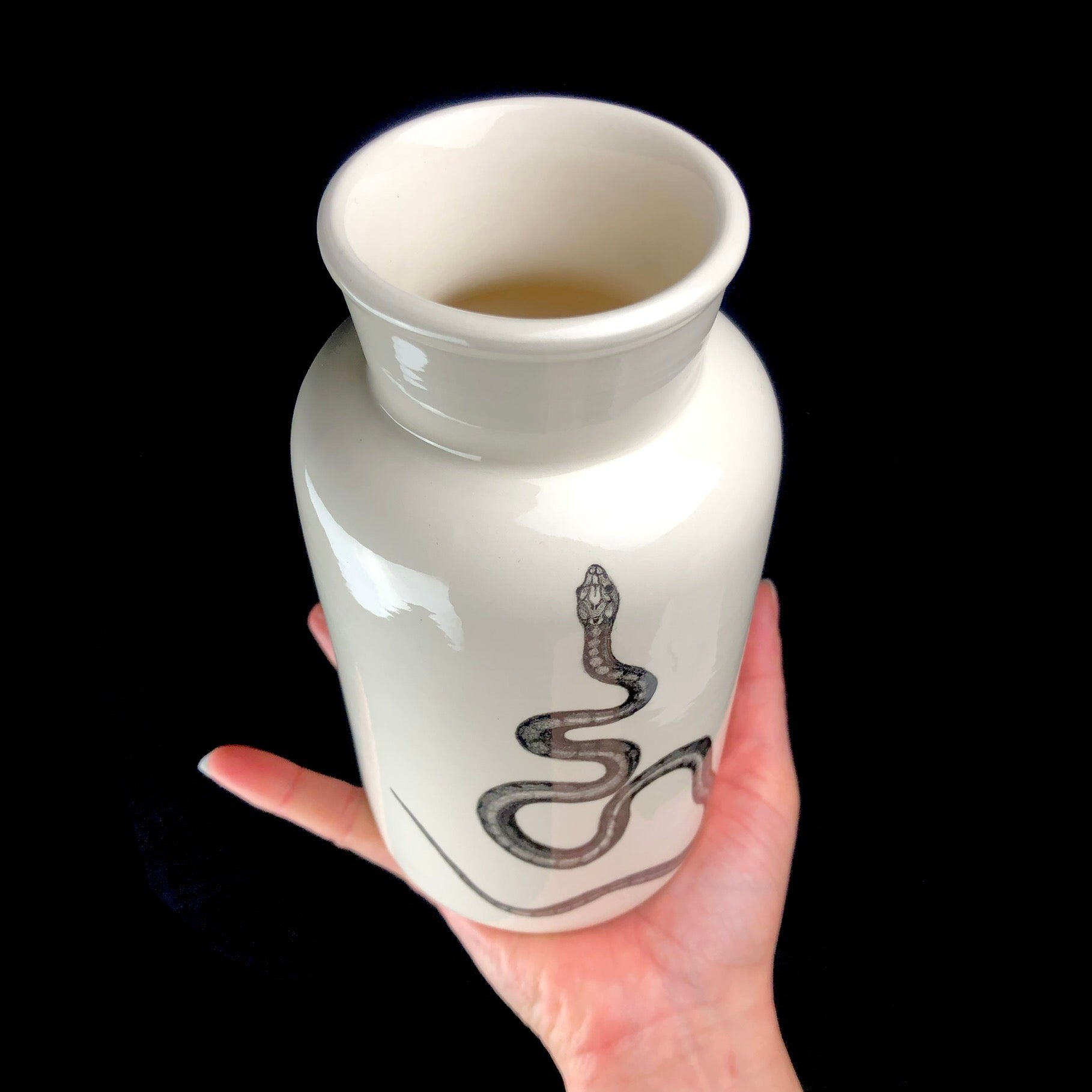 Top view of white vase with snake image shown held in hand.