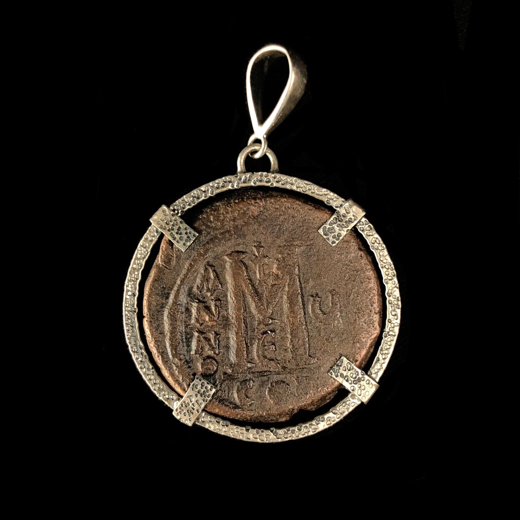 Bronze colored coin with the  latter M surrounded by characters 
