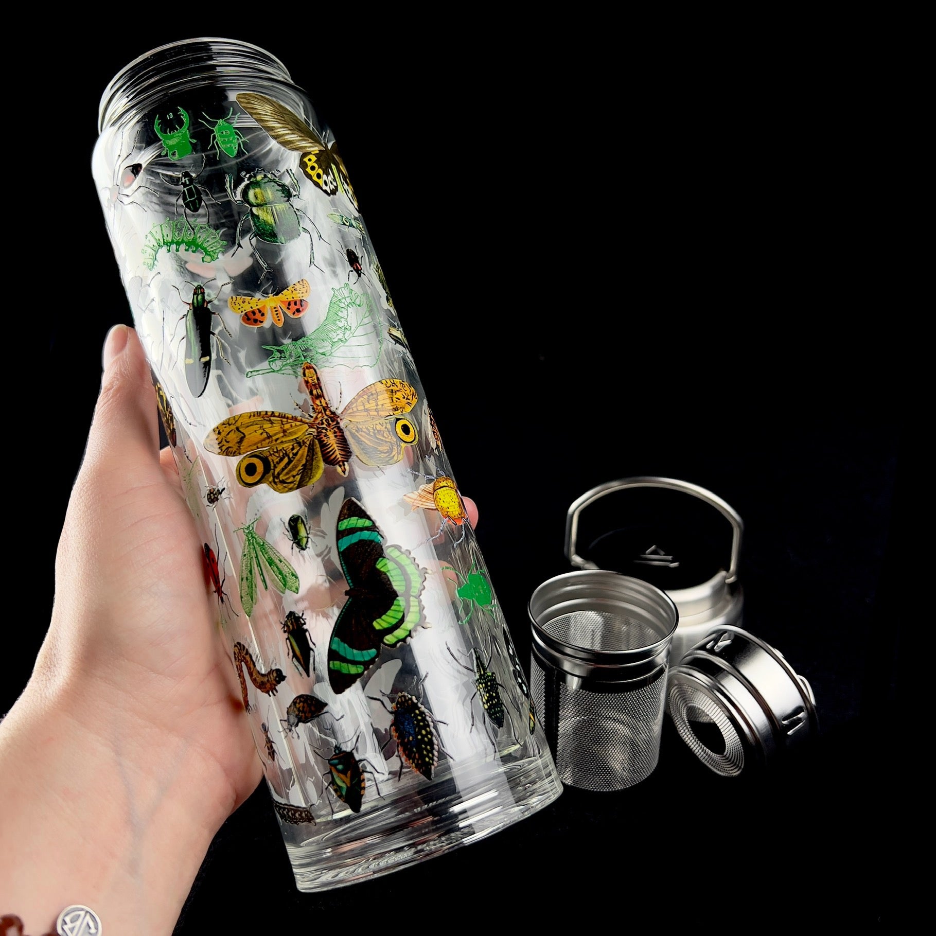 Entomology Tea Infuser shown in hand with basket and lid in background