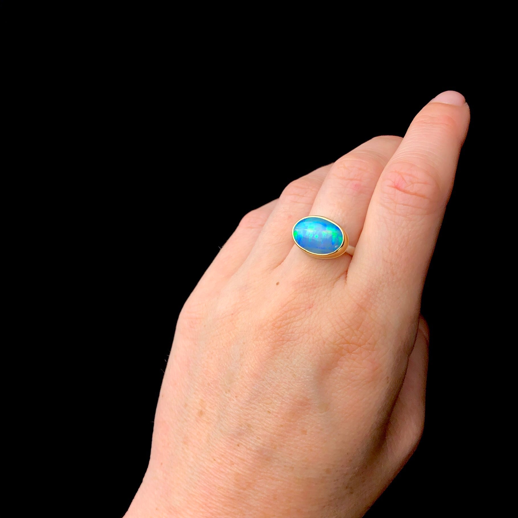 Blue and green jelly opal ring shown on hand