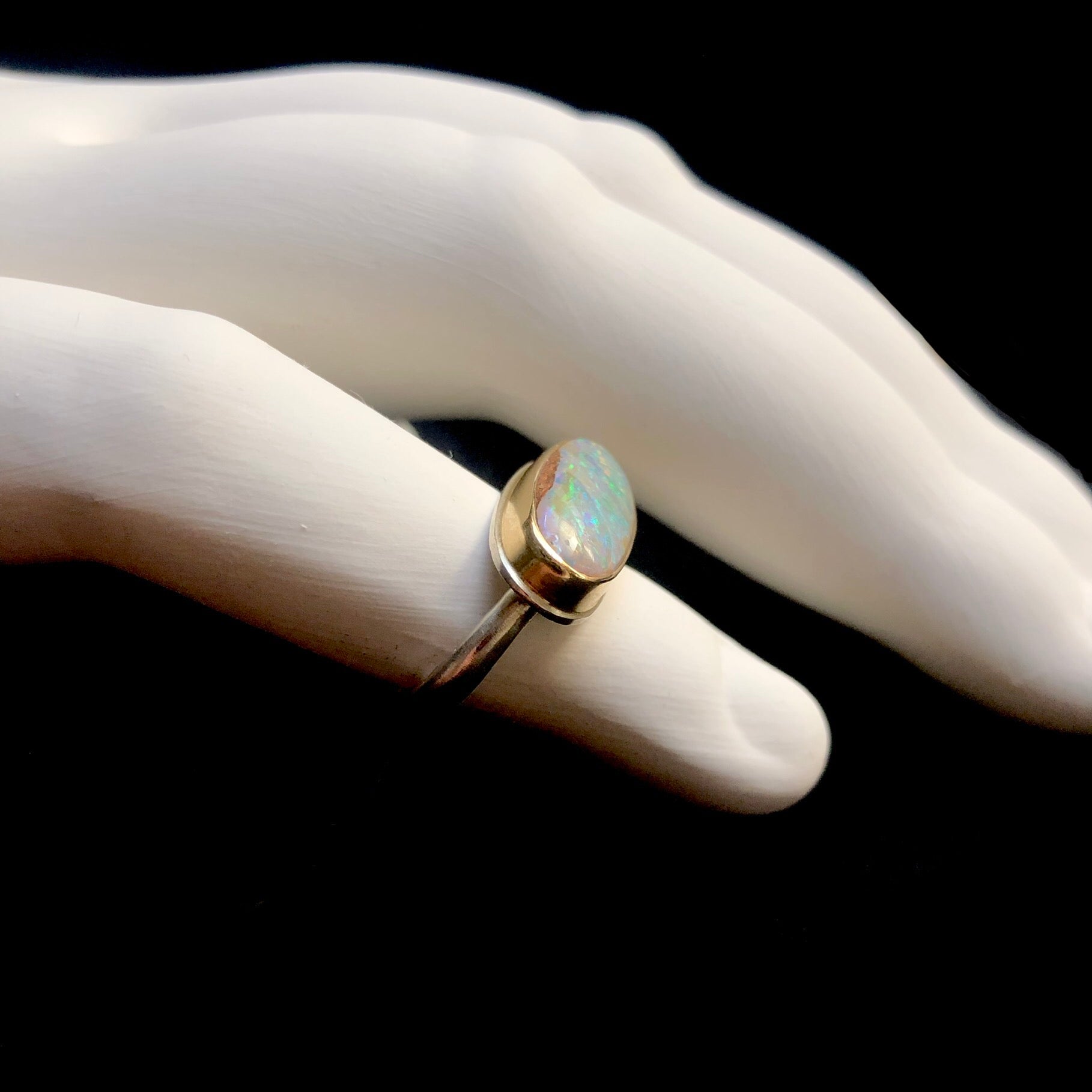 Side view of Fossilized Opalized Wood ring with gold setting and silver band on white ceramic finger