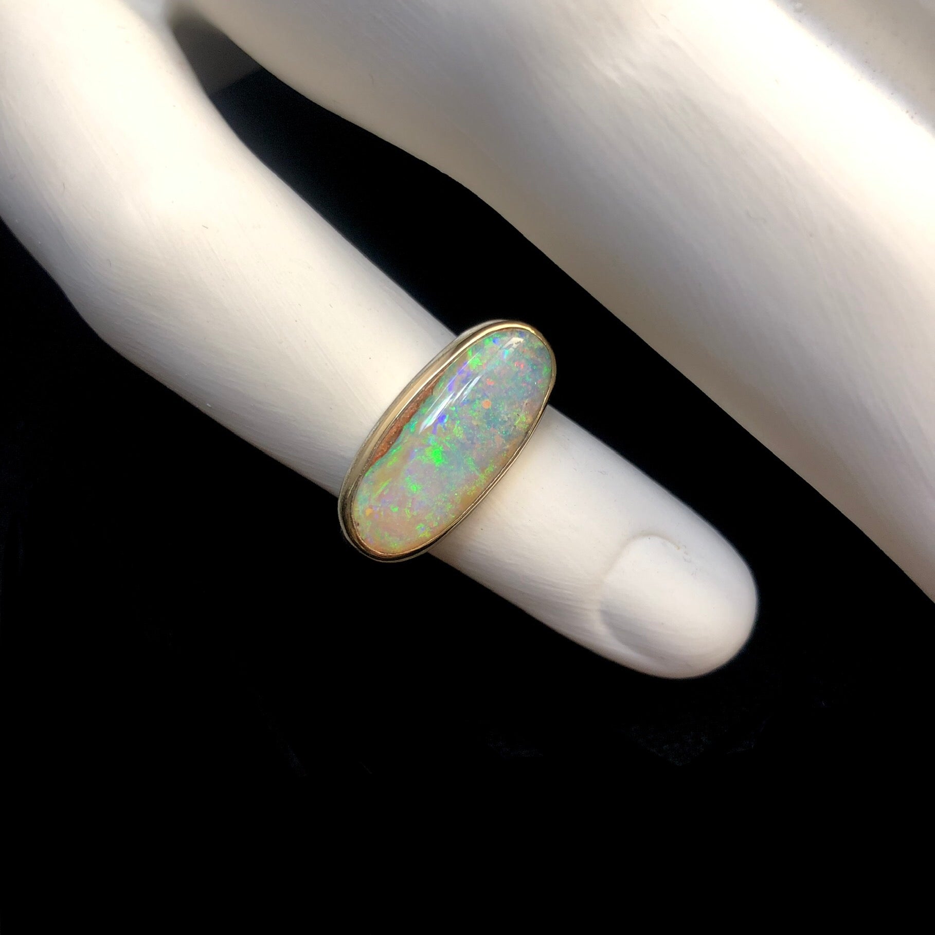 Iridescent green, violet purple and pink confetti of color in opal stone ring shown on white ceramic finger