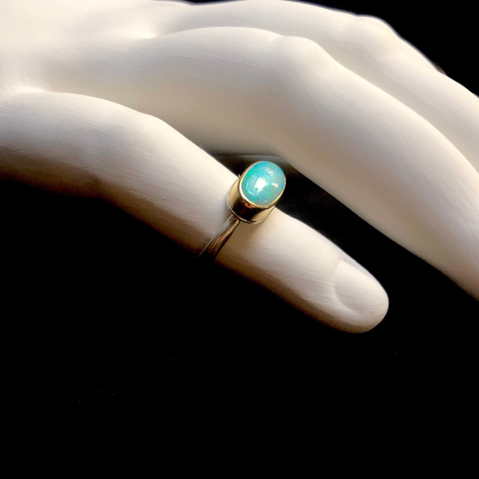 Side profile view of smooth greenish blue stone ring with gold setting and silver band shown on white ceramic finger