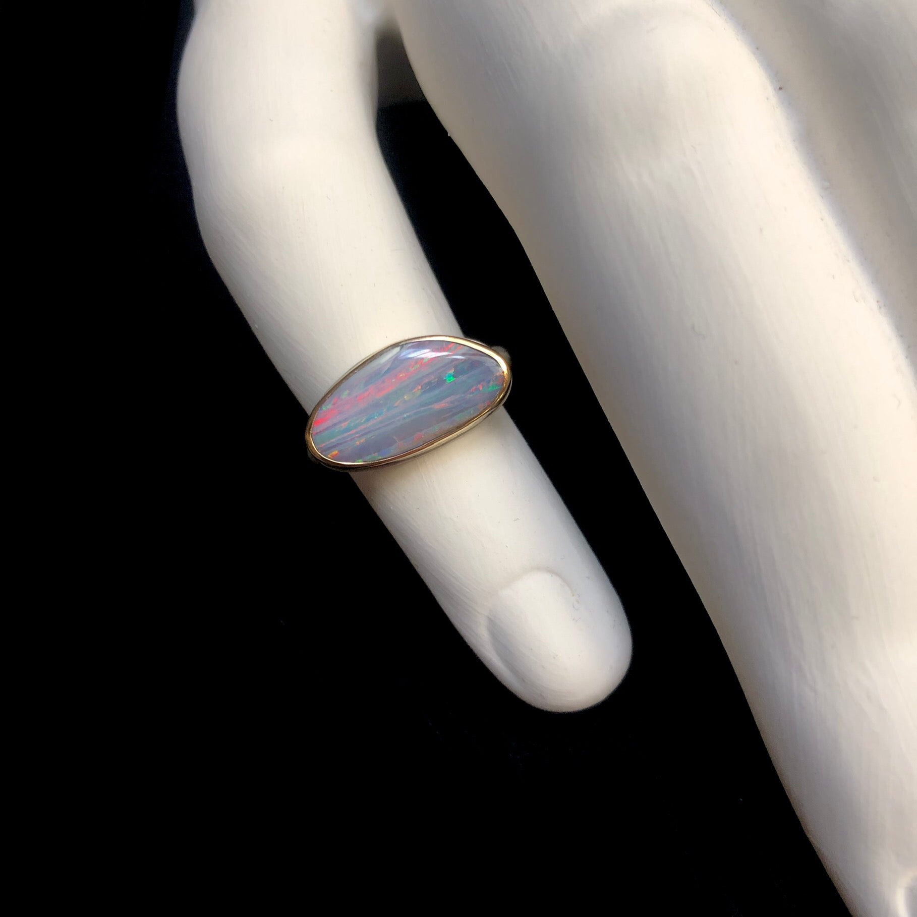 Lowly lit Boulder opal ring with smokey lilac grey overtones of color shown against white ceramic finger