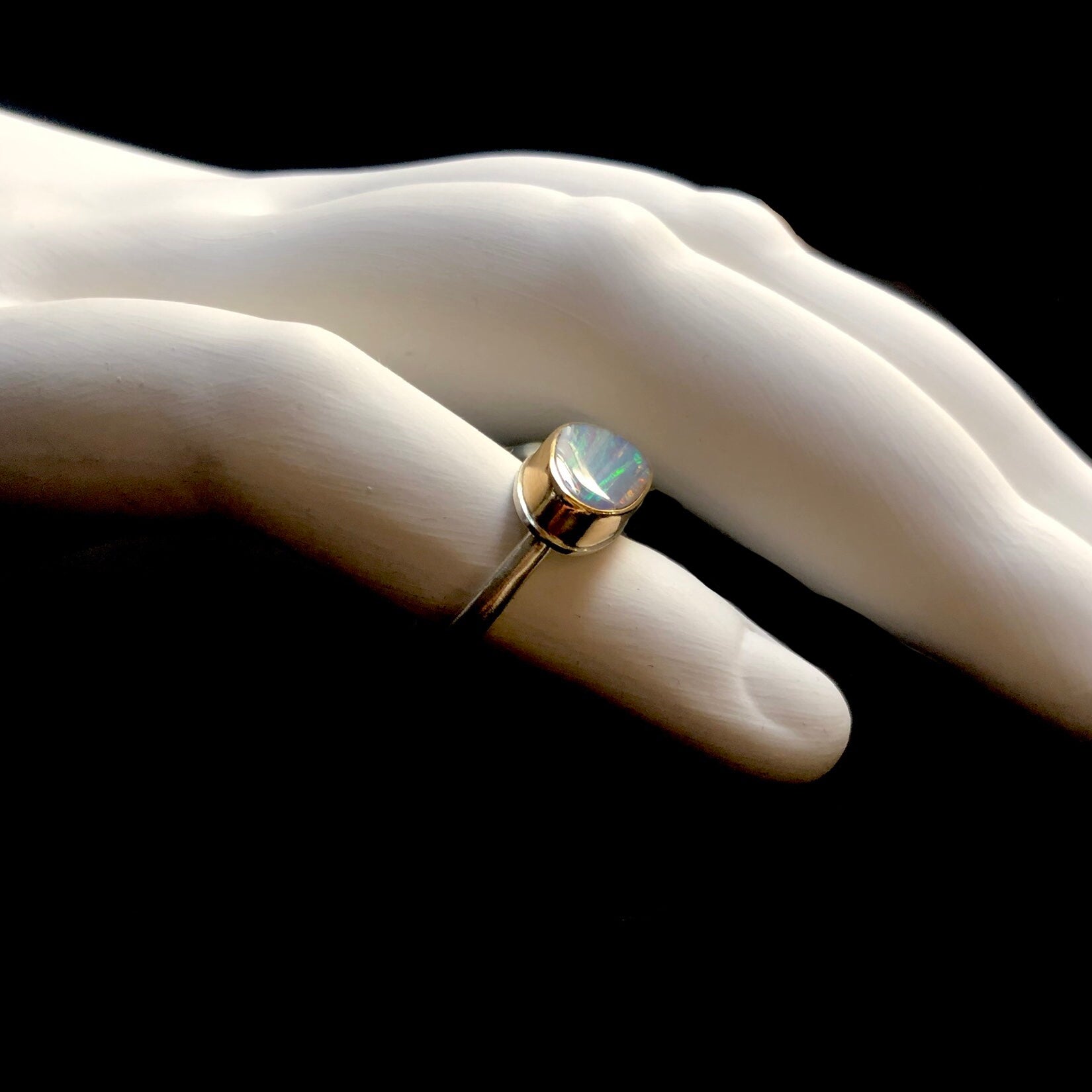 Side profile view of boulder opal ring with gold setting and silver band shown on white ceramic finger