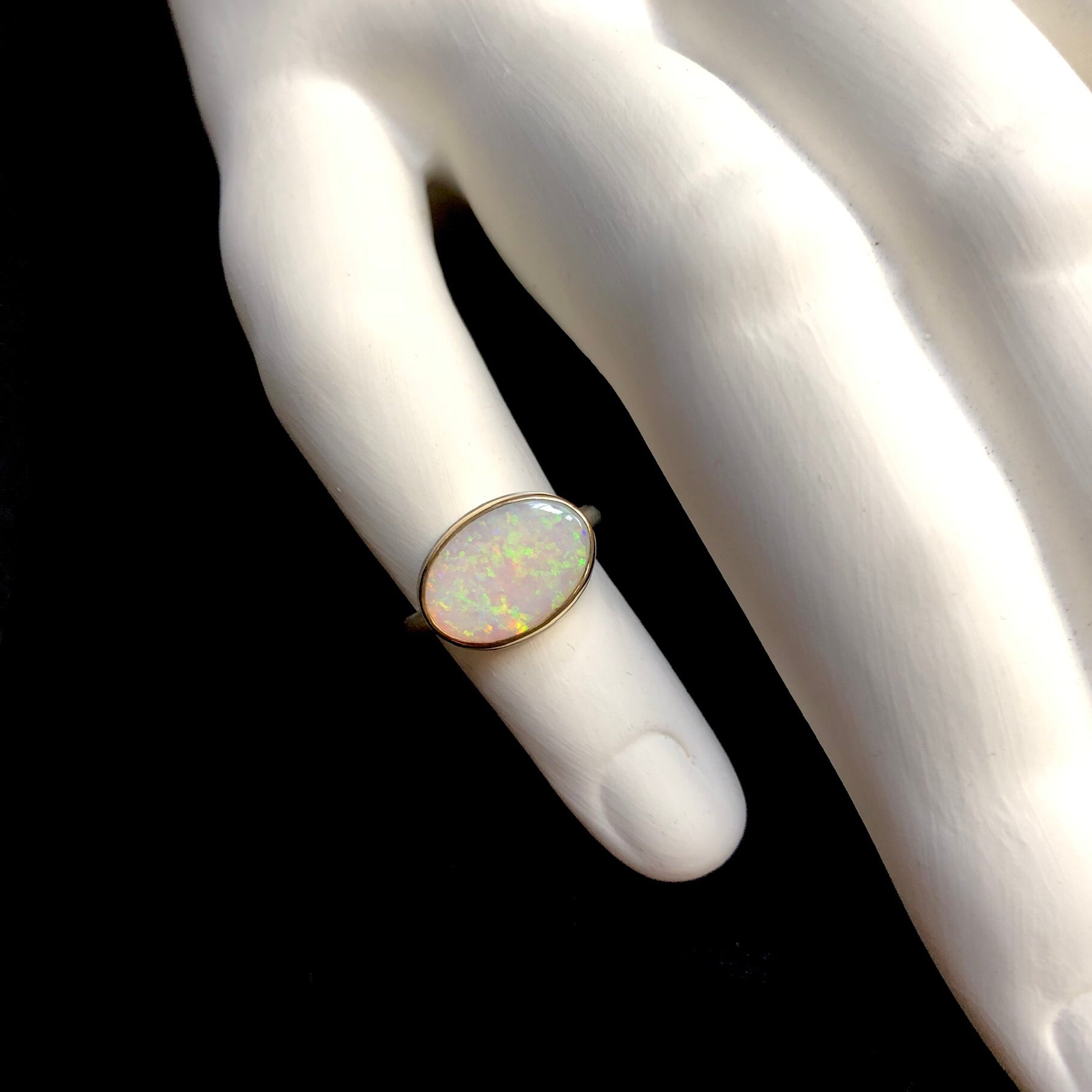 Top view of oval iridescent white colored Mintabe Opal ring on white ceramic finger