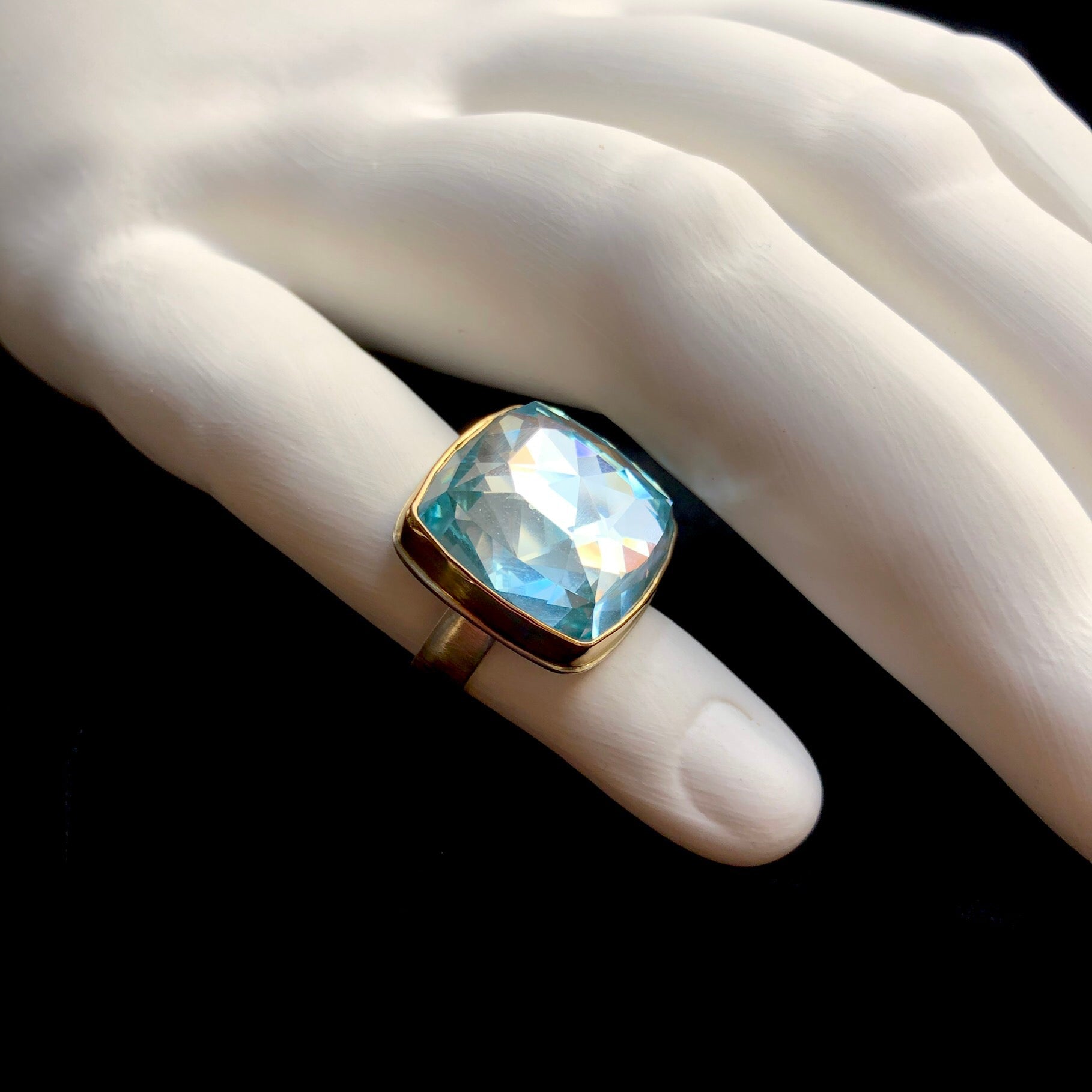 Side profile view of Blue Topaz Ring with gold setting and band on white ceramic finger