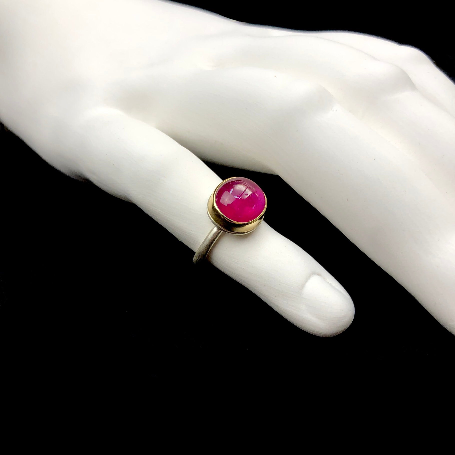 Side profile view of polished surface of pink ruby stone ring shown on white ceramic finger